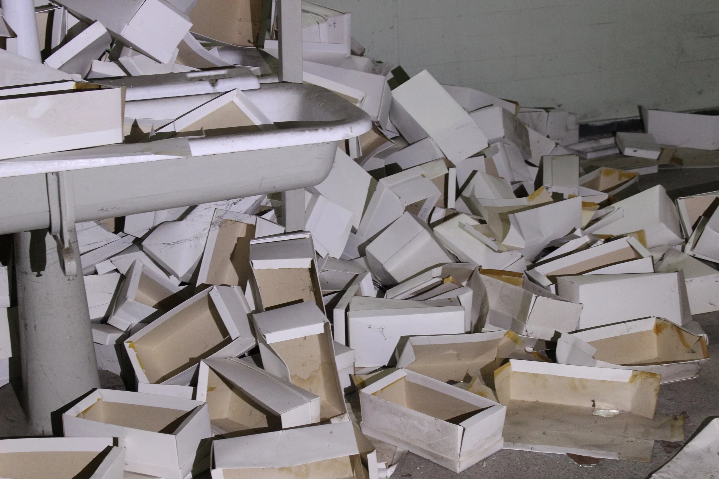 Viele umgestürzte weiße Kartons auf einem Boden, neben einer alten Badewanne.