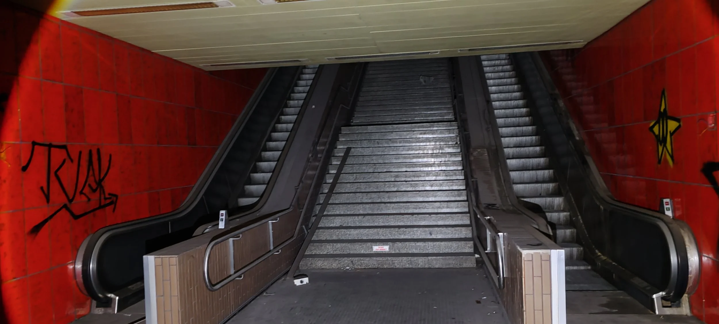 Leeres Treppenhaus mit rolltreppe und Wand mit Graffiti in einem öffentlichen Gebäude.