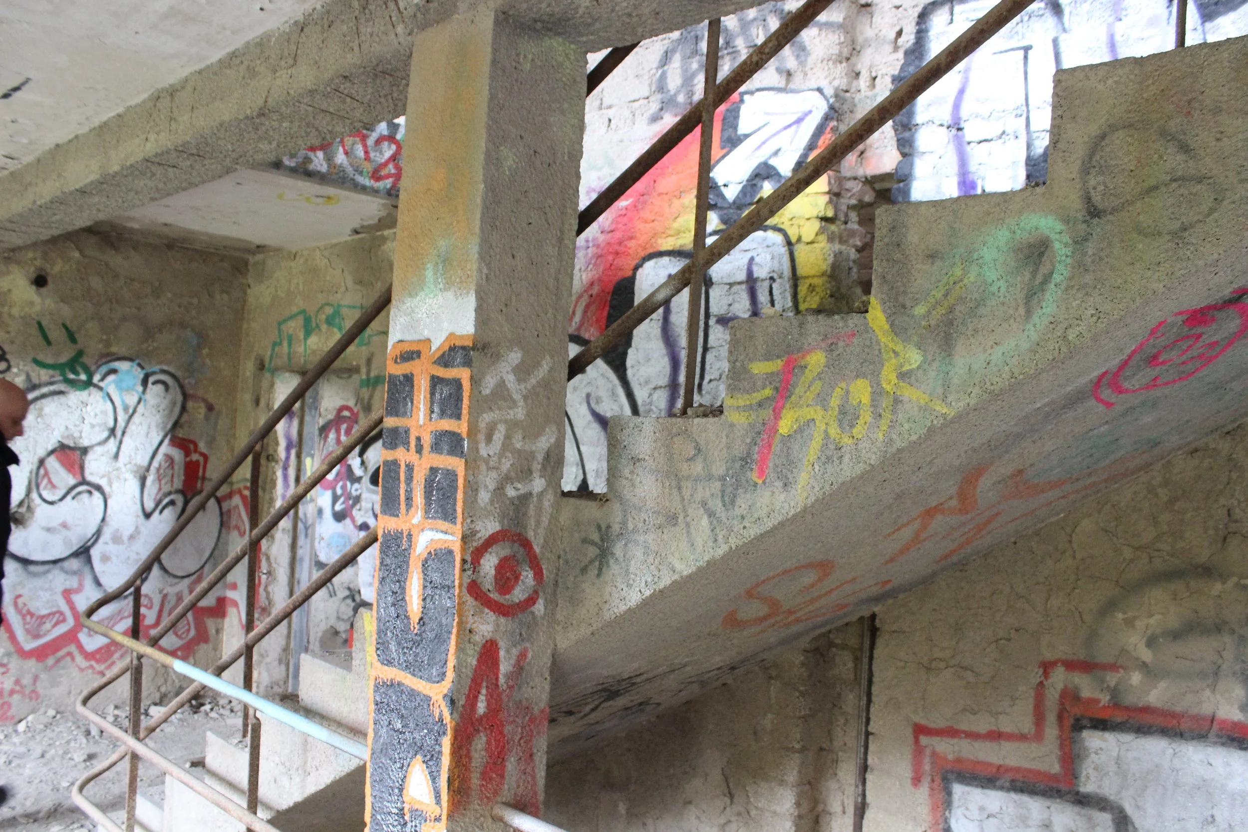 Innenansicht eines zerstörten Gebäudes mit urbaner Graffiti-Kunst an den Wänden, einer Treppe und einem Eisenhandlauf.