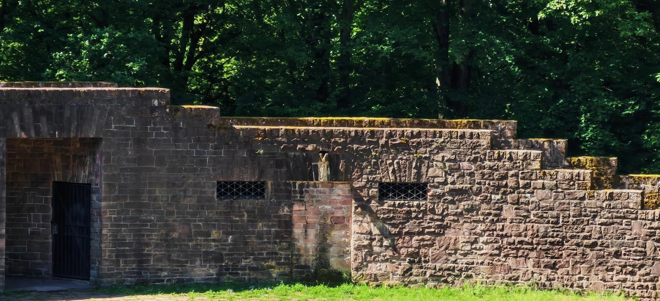 Eine historische Backstein-Festung mit Stufen auf dem Dach, an der Seite eines grünen Waldes.