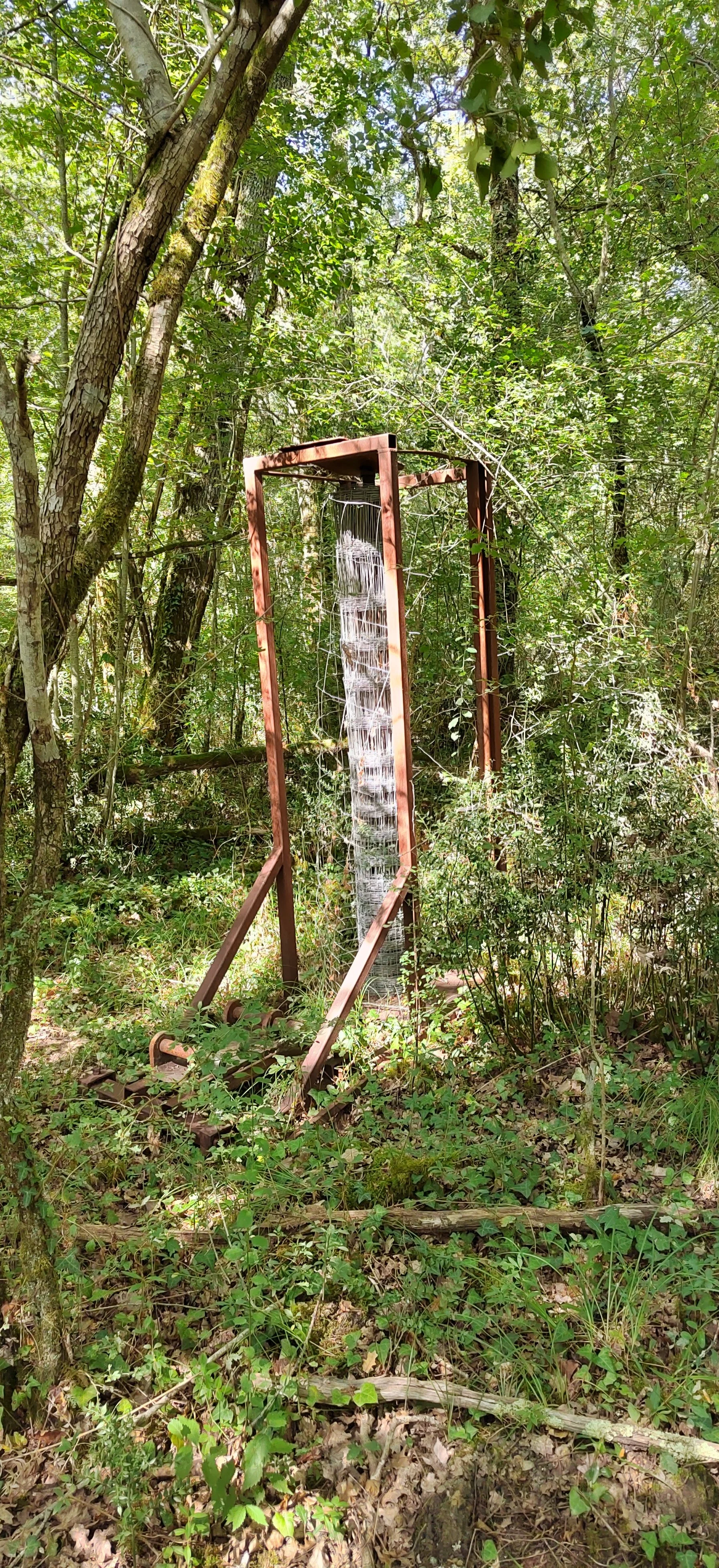 Ein Wildwasserbahn-Attraktion, die im Wald steht, besteht aus einem Metallrahmen mit Wasser flowing nach unten, umgeben von Bäumen und Buschwerk.