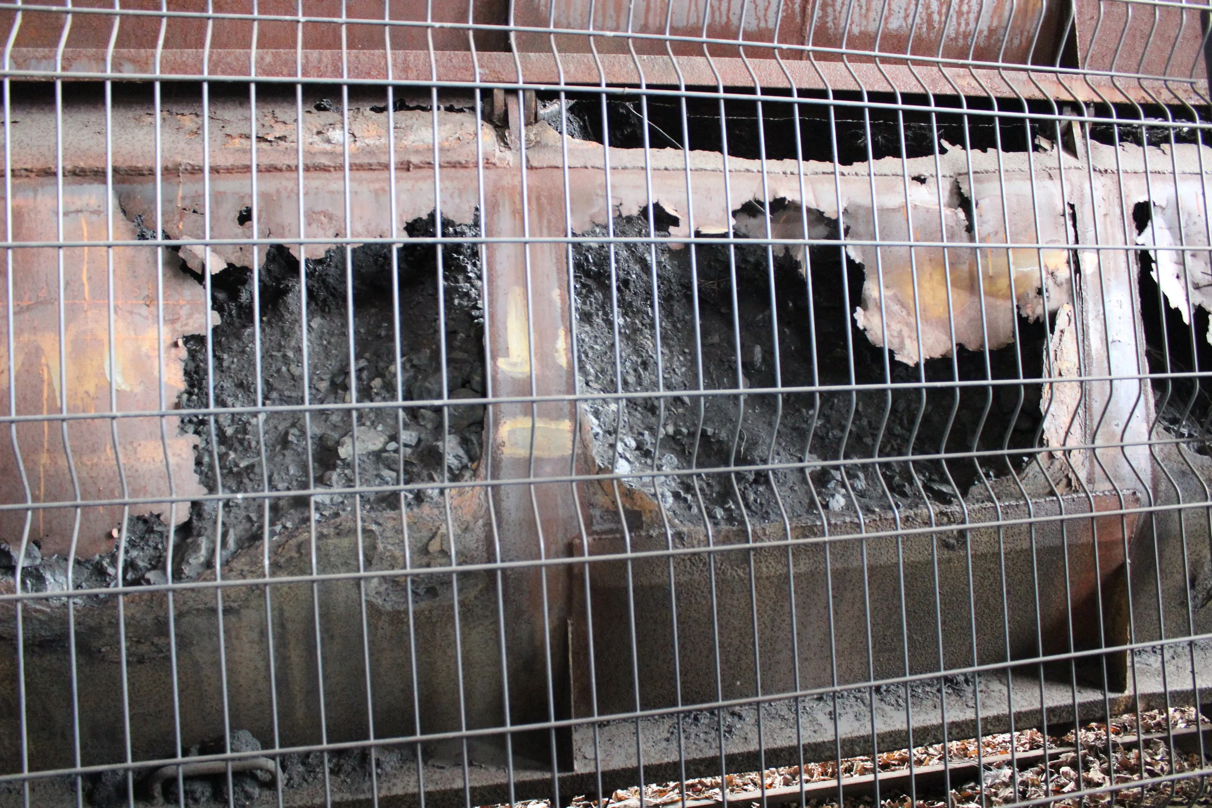 Brennender Eisenofen mit Пепел und Asche, hinter einem Metallzaun