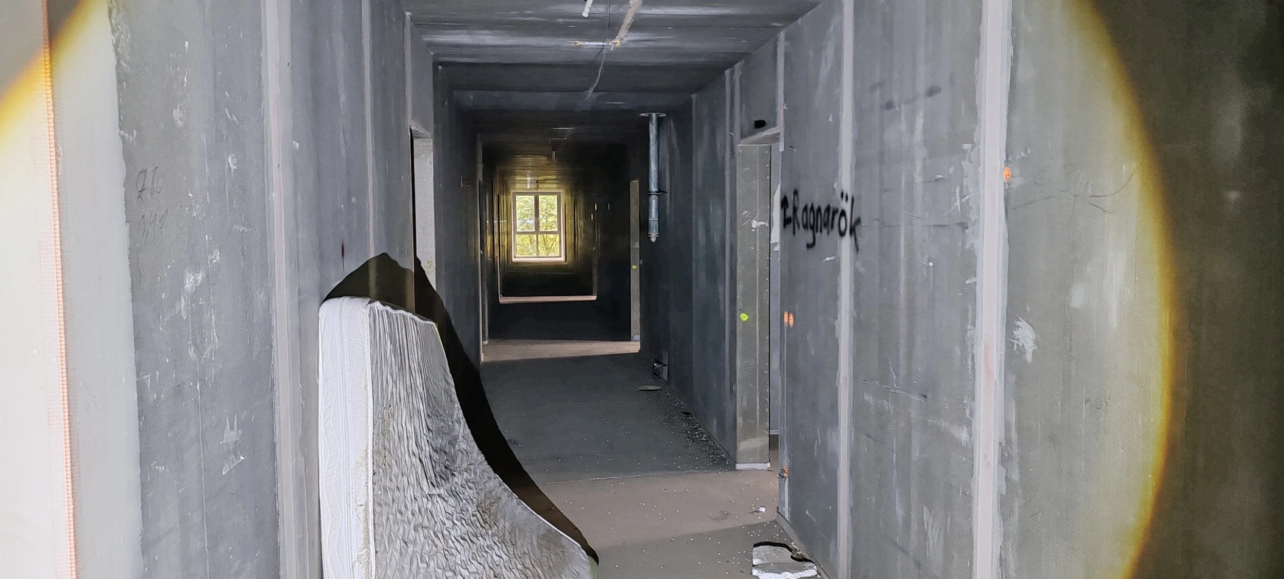 Innenansicht eines unvollendeten Gebäudes mit grauen Wänden, einem Fenster am Ende des Korridors und Graffiti an der Wand auf der rechten Seite.