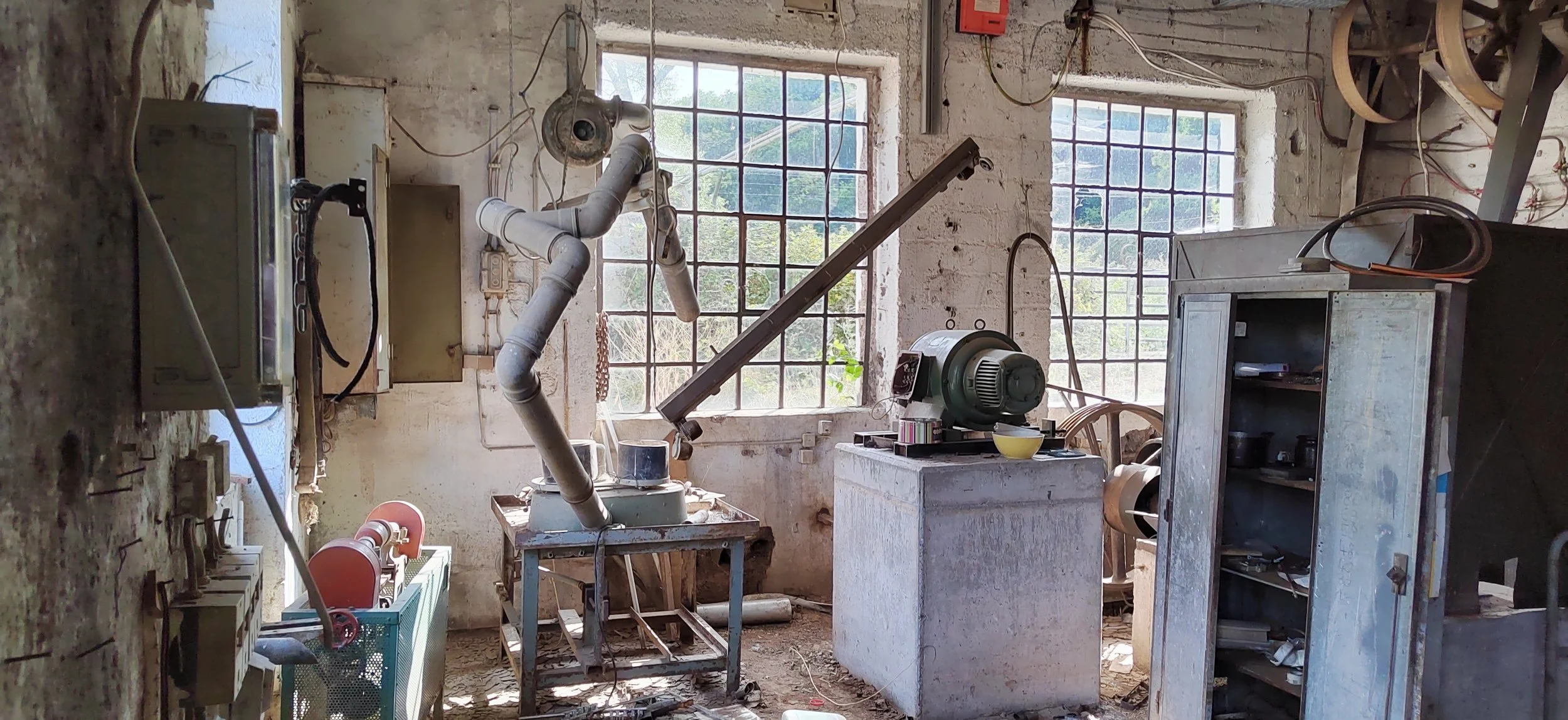 Ein alter, verlassener Werkstattraum mit alten Maschinen, Werkzeugen und zerbrochenen Fenstern, viel Schmutz und Staub auf dem Boden.