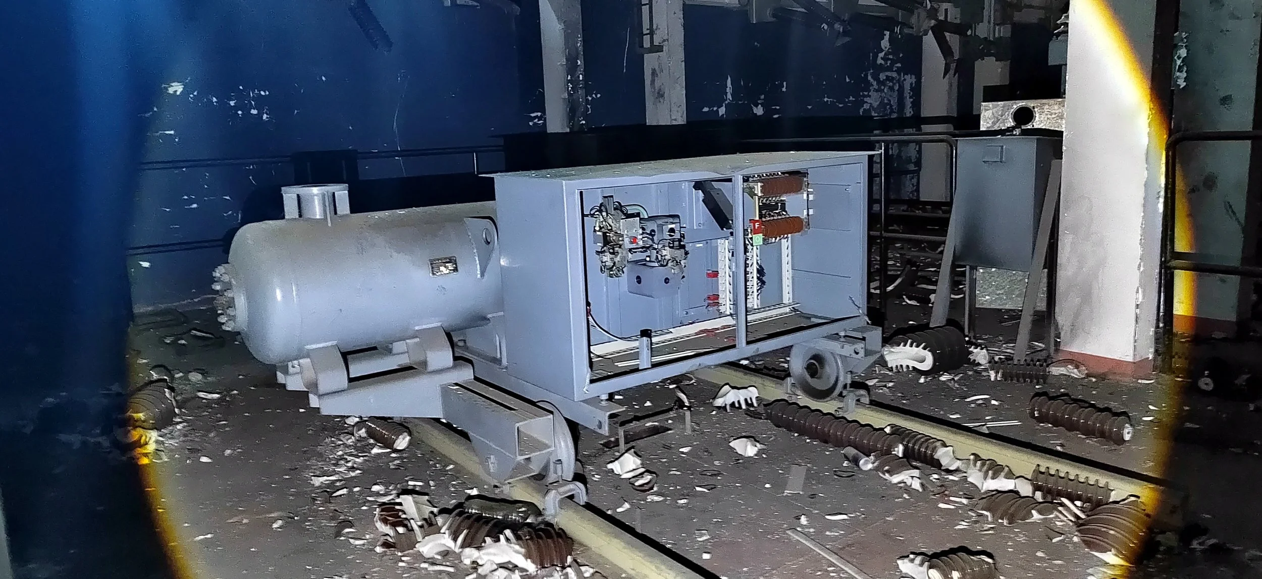 Zerstörtes maschinelles Gerät auf der Bahnstrecke in einem dunklen Raum, umgeben von Trümmern und Schutt.