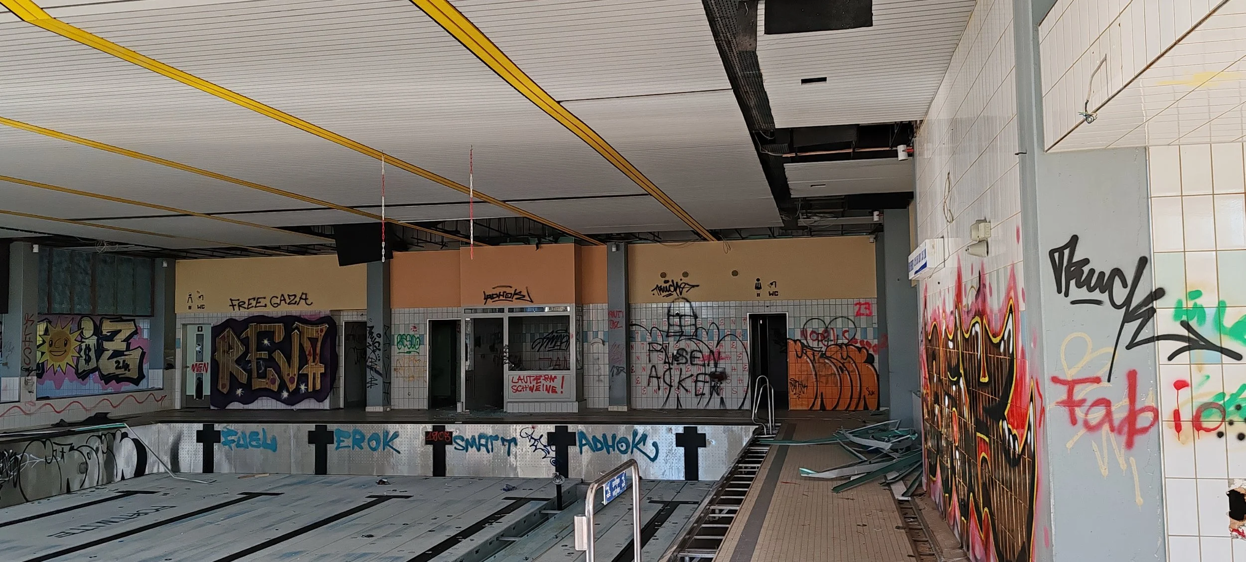 Ehemaliges, destruidos Schwimmbad mit Graffiti an den Wänden, verfallene Schwimmbecken, zerstörte Fliesen und verwehte Gegenstände