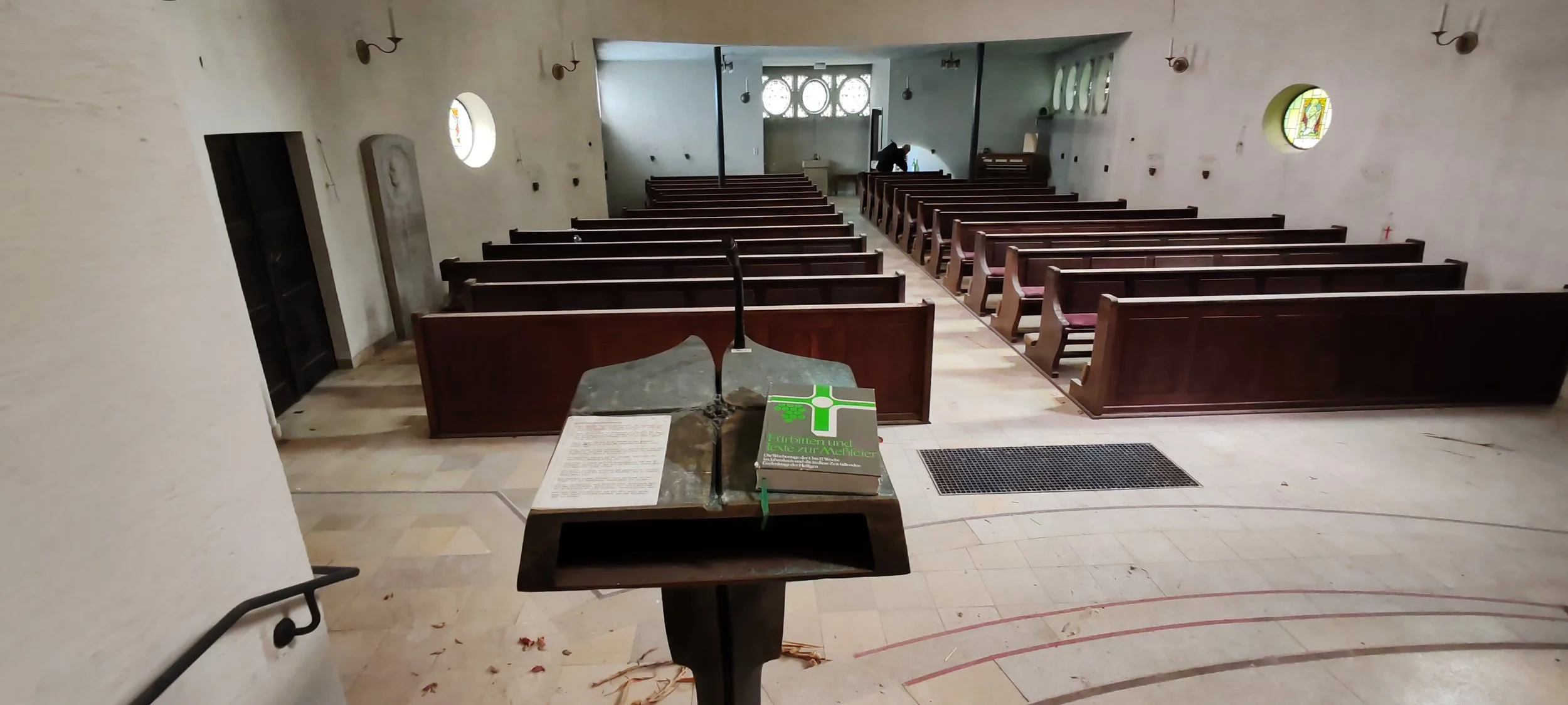 Innenansicht einer leeren Kirche mit Holzbänken, einem Altar, einer ausgestellten Bibel und einem Rednerpult.