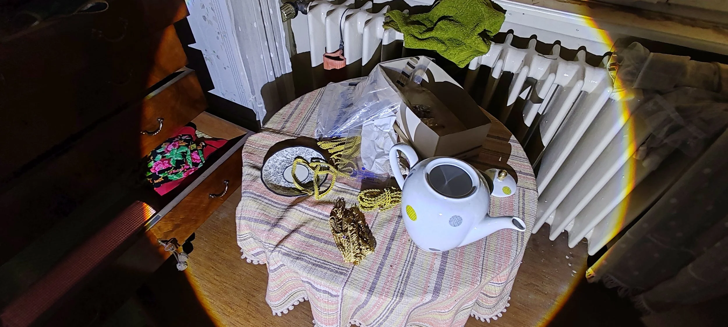 Ein Tisch mit einer Teekanne, Geschenkpapier, Schnur und Papier. Im Hintergrund eine Heizung und ein dunkles Möbelstück.