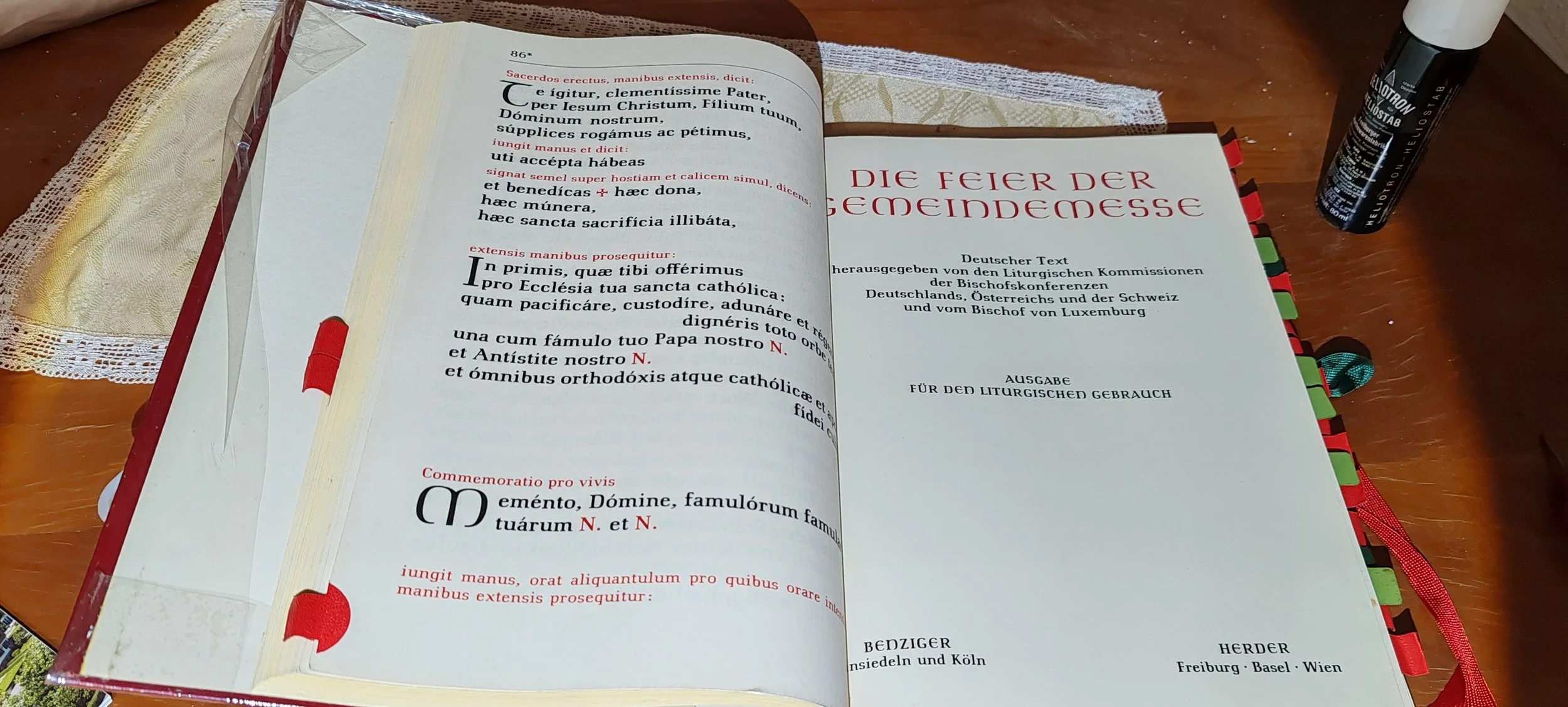 Ein aufgeschlagenes Buch, das den deutschen Text der Feier der Gedenkmesse zeigt, mit bunten Registerkarten am Rand, auf einem Holzschreibtisch mit einem schwarzen Marker und einem Cocktail, der auf der rechten Seite liegt.