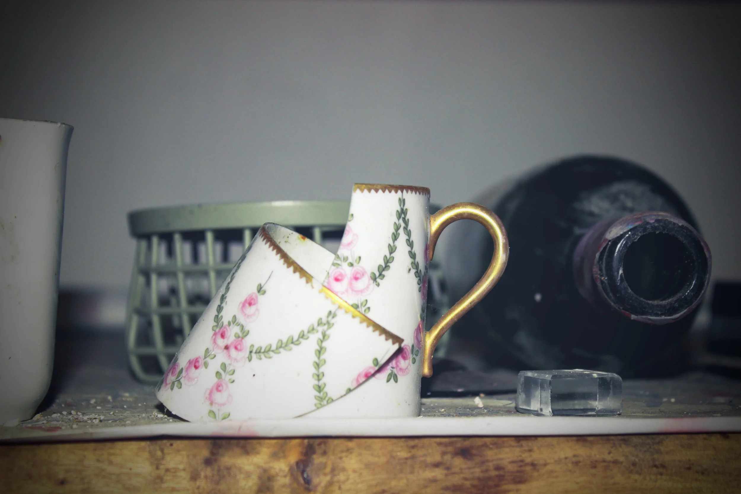 Zerbrochene Porzellantasse mit rosa Blumendekor, auf einer Holztischplatte