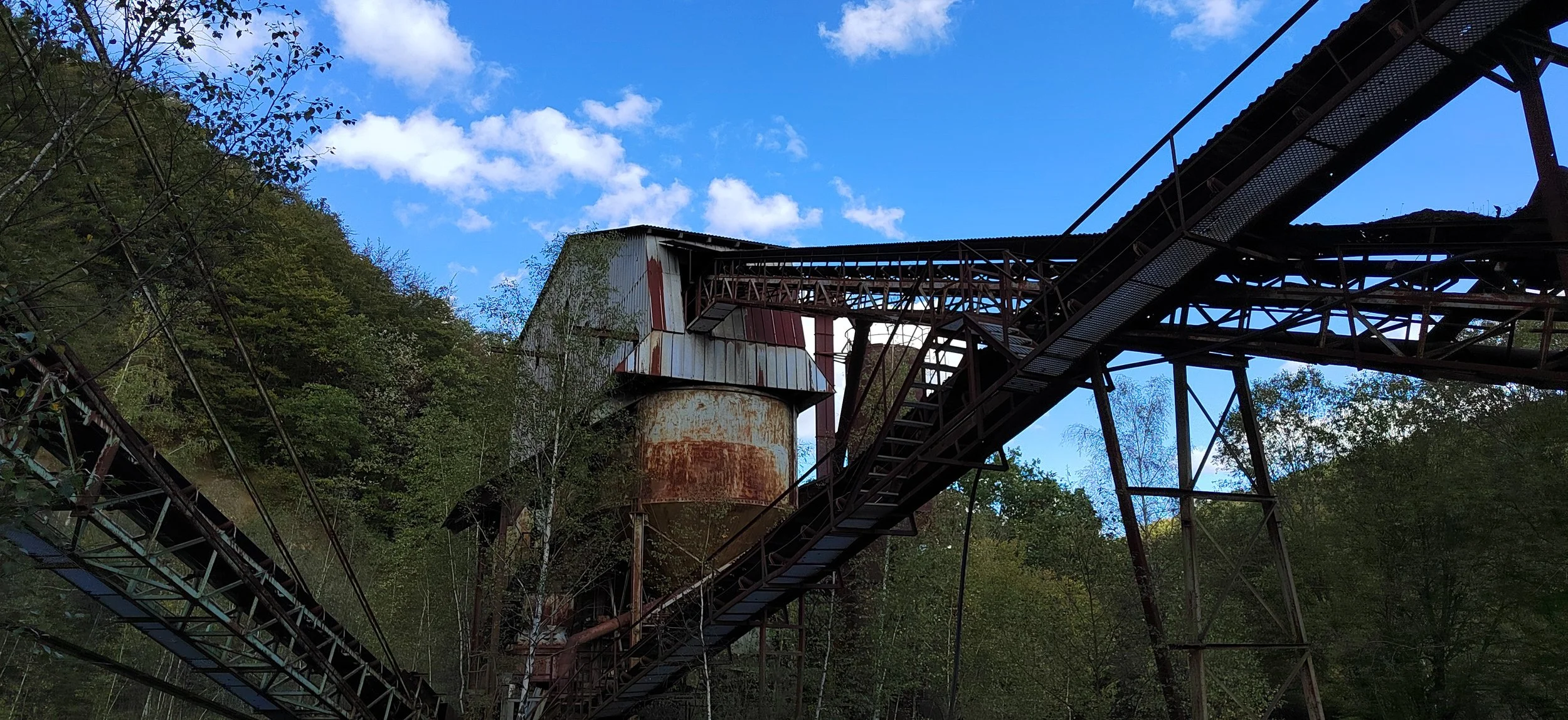 Verrostete interstation (oben, Mitte), überdachte, schmale, steile eisernes Treppe, inmitten von grünen Bäumen, blauer Himmel mit Wolken.