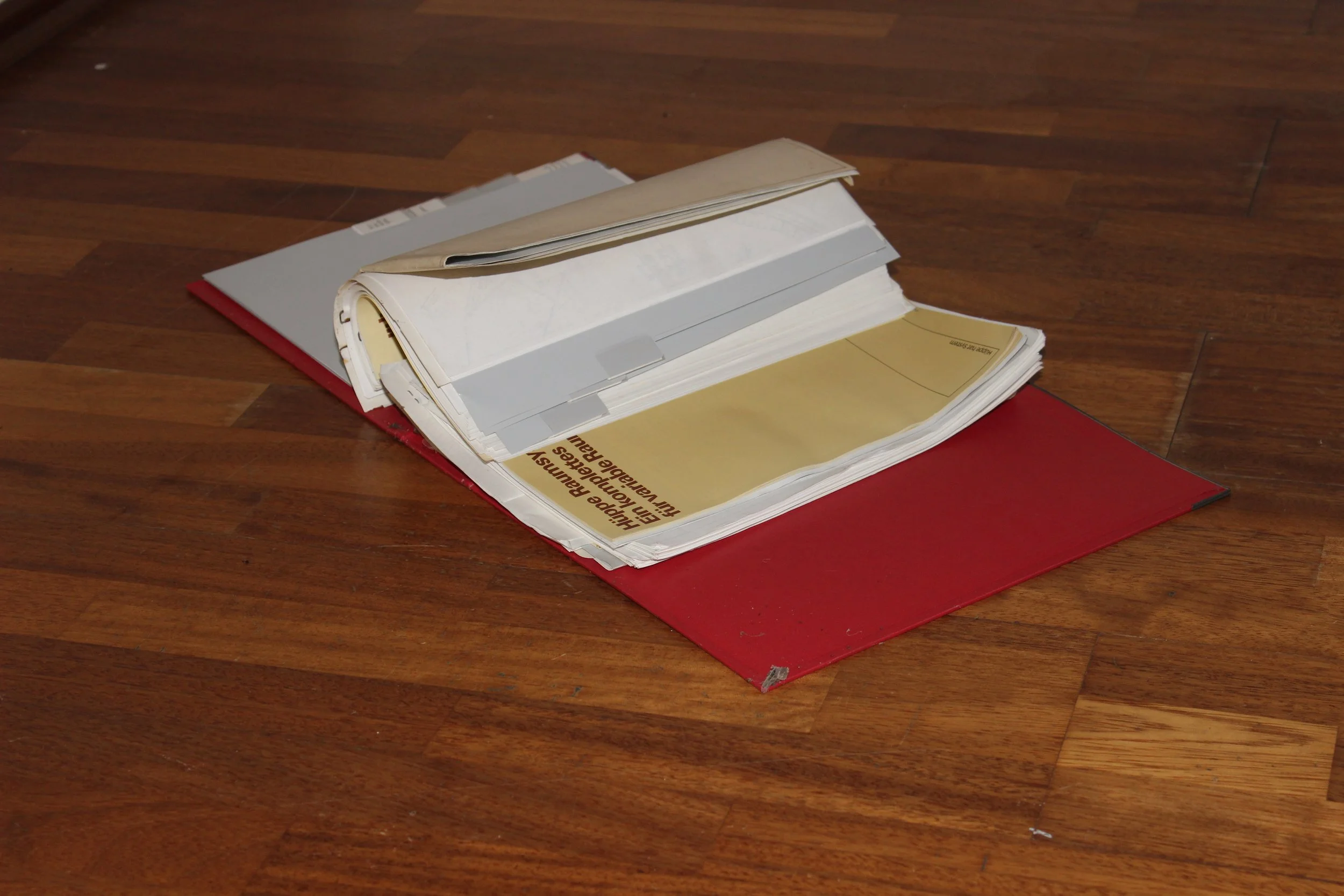 Offenes Aktenordner auf Holzboden, mit Dokumenten und Papieren darin.