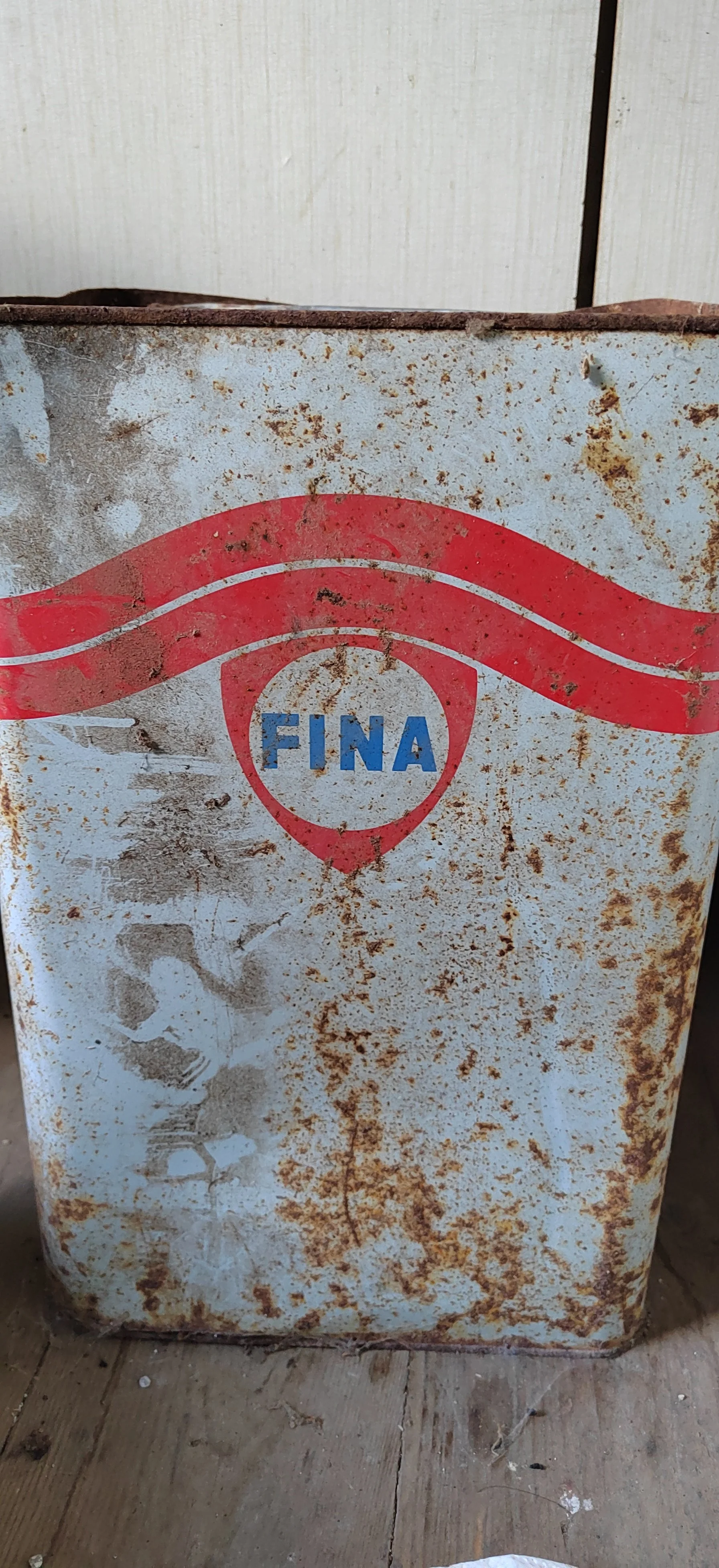 Ein rostiger, alter Getränkekasten mit der Aufschrift 'FINA' auf einem Holzfußboden.
