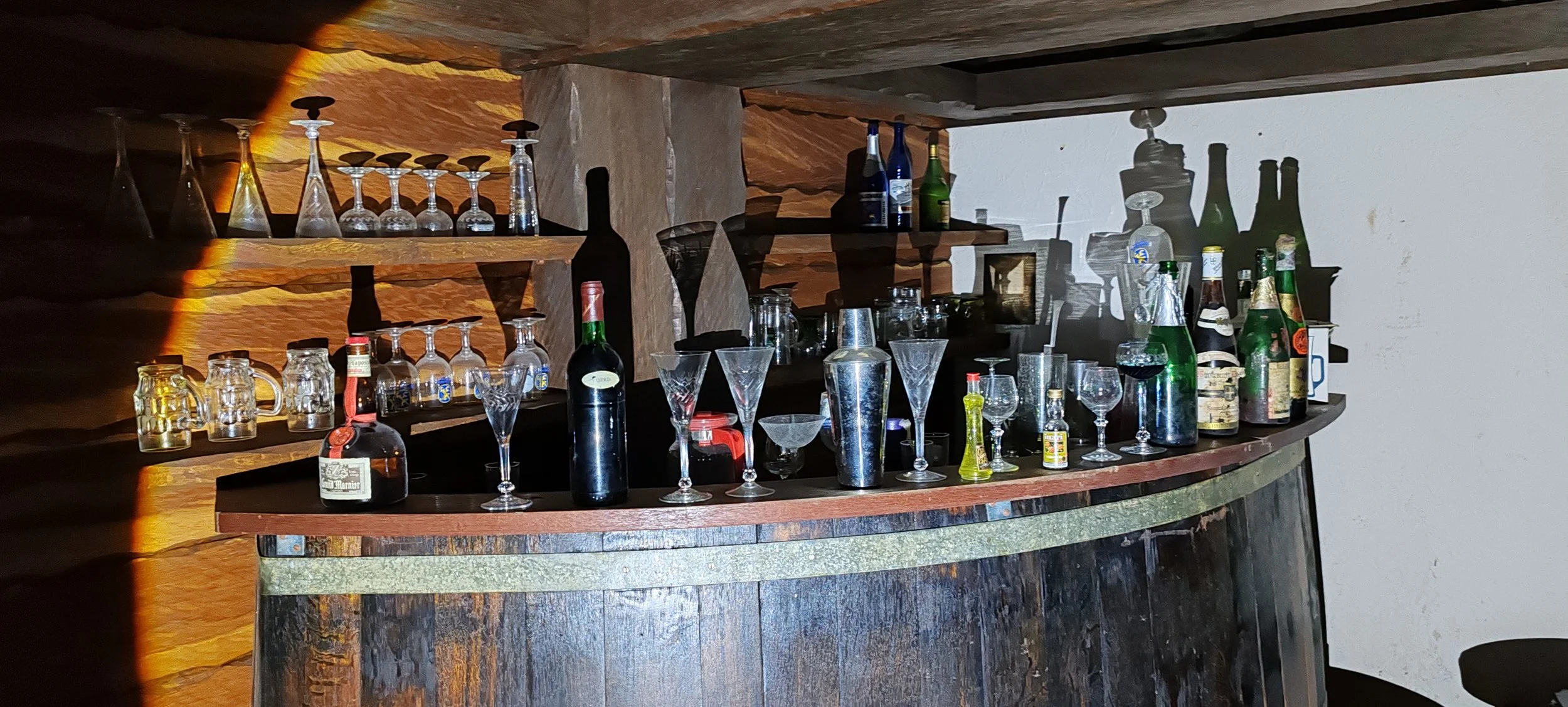 Barmöbel mit verschiedenen Alkoholflaschen, Gläsern und Dekorationen auf Holzregalen und Theke.