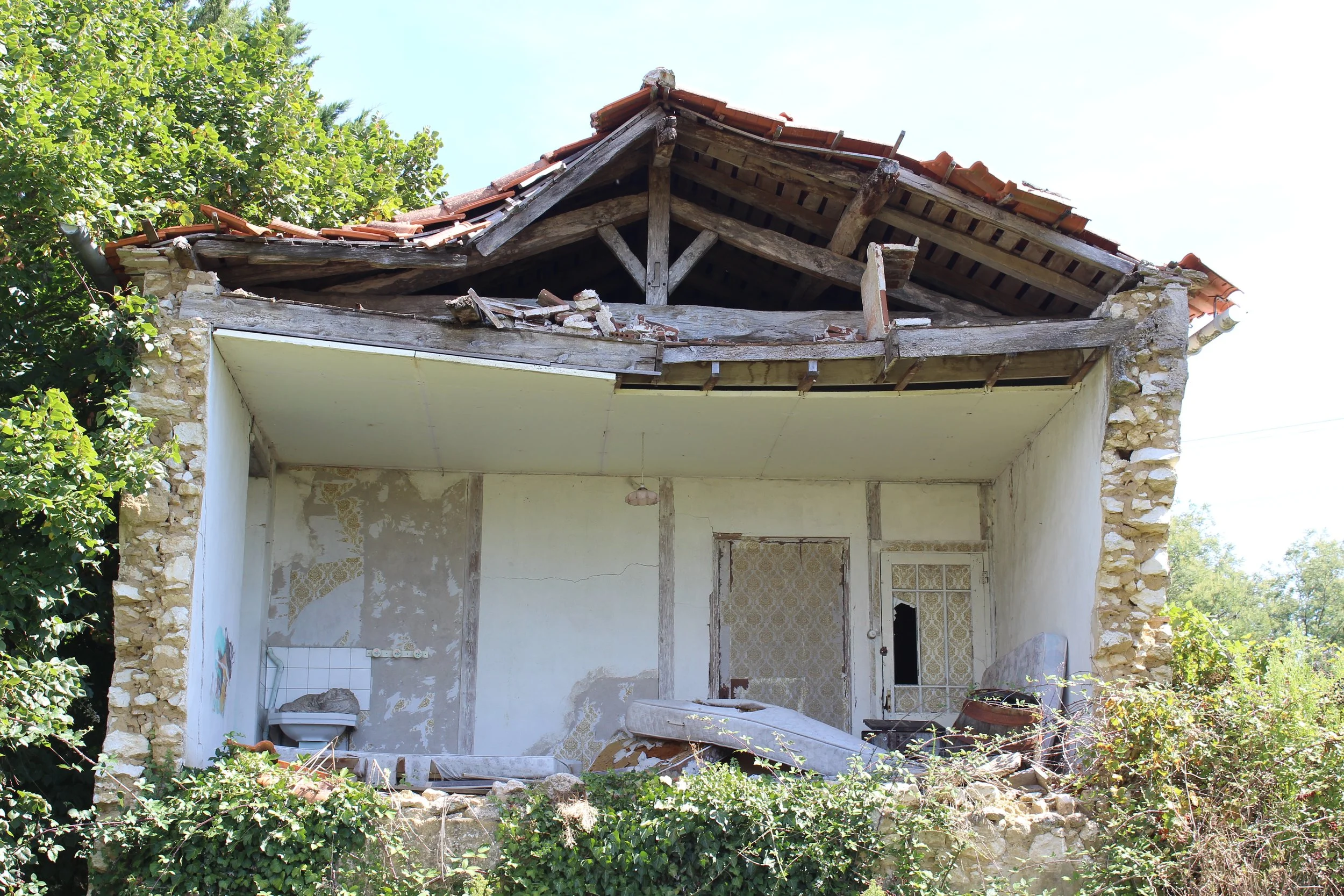 Ein verfallenes, einst bewohnbares Haus mit zerstörtem Dach, überwuchert von Pflanzen