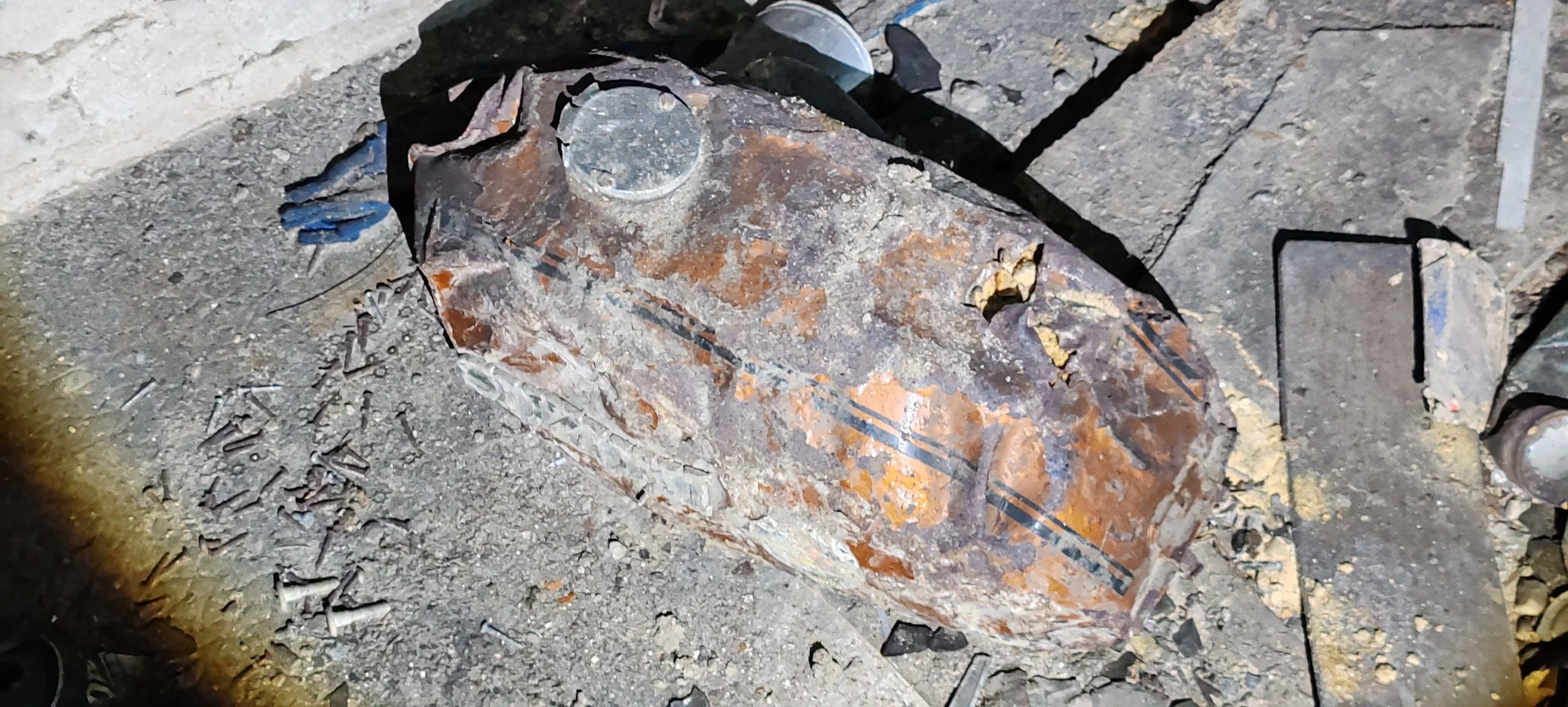 Ein alter, beschädigter metallischer Gegenstand auf einem Boden, umgeben von Trümmern und Staub.