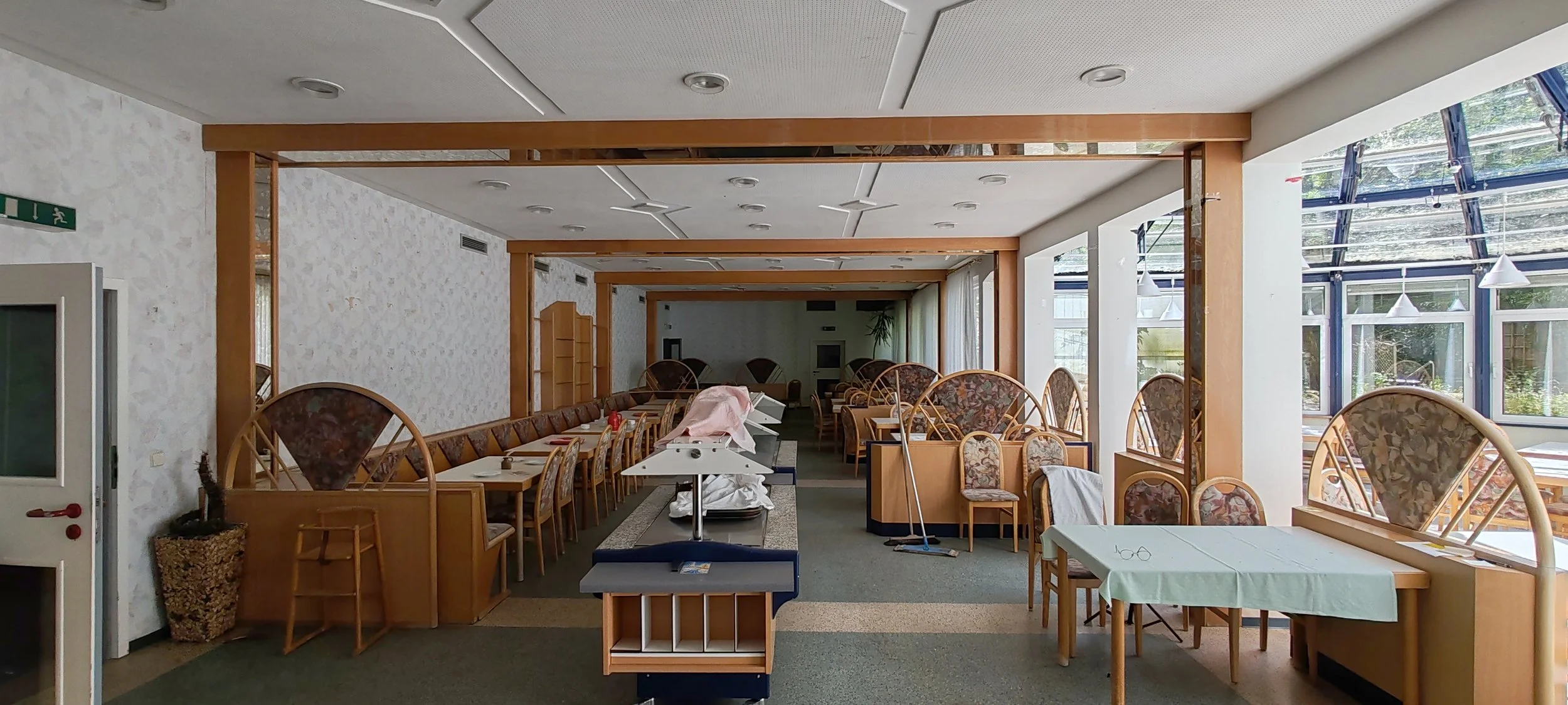 Leeres Restaurant mit Tischen und Stühlen, große Fenster, dekorative Holzrahmen, aufgeräumt, mit Sonnenlicht, im Hintergrund Pflanzen