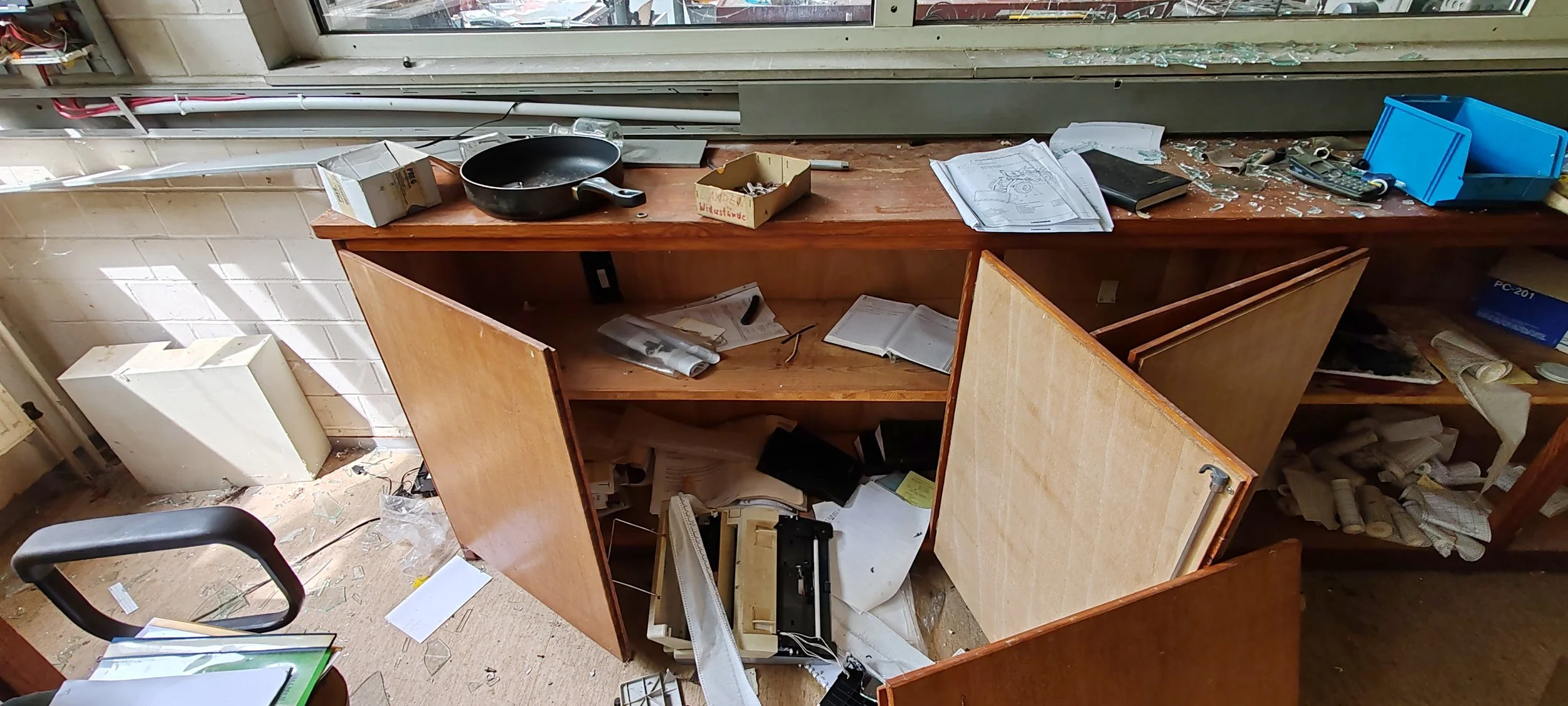 Room mit zerbrochenen Schränken und zerstreutem Papier, Werkzeug und Büchern.