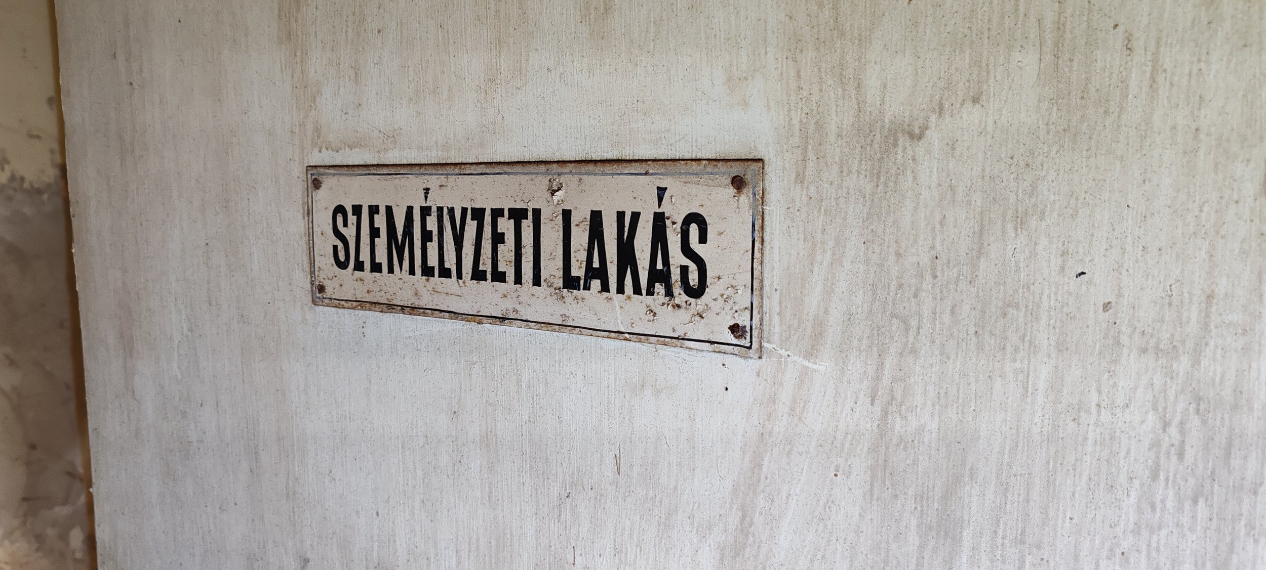 Metallschild mit der Aufschrift 'Személyzeti Lakás', an einer weißen Wand.