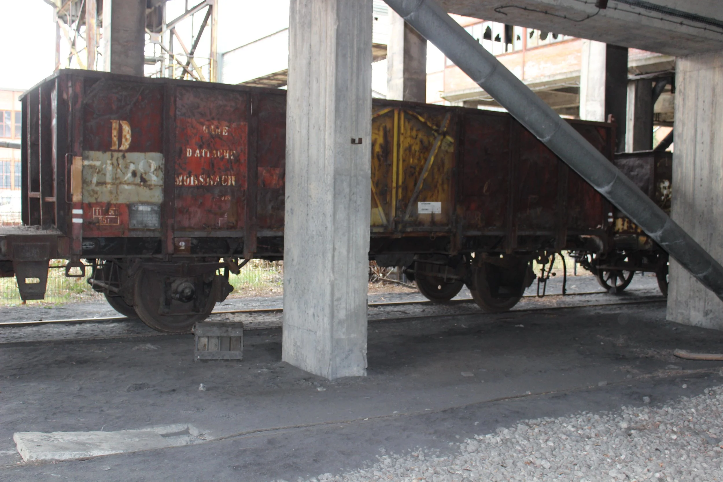 Ein alter, verrosteter Güterwagen auf einem Eisenbahngleis, umgeben von Baustellenelementen und unbefestigtem Boden.