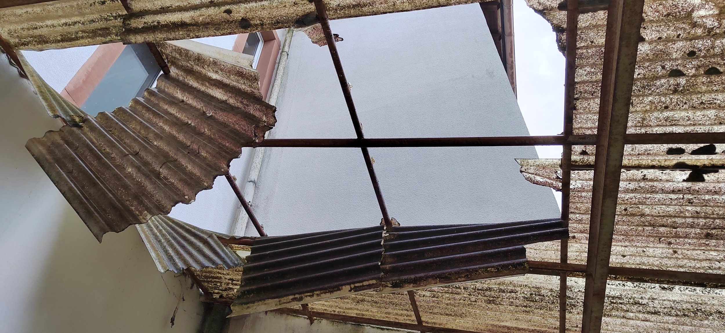 Verrostete, zerbrochene Wellbleche an einem alten Dach mit Metallstangen.