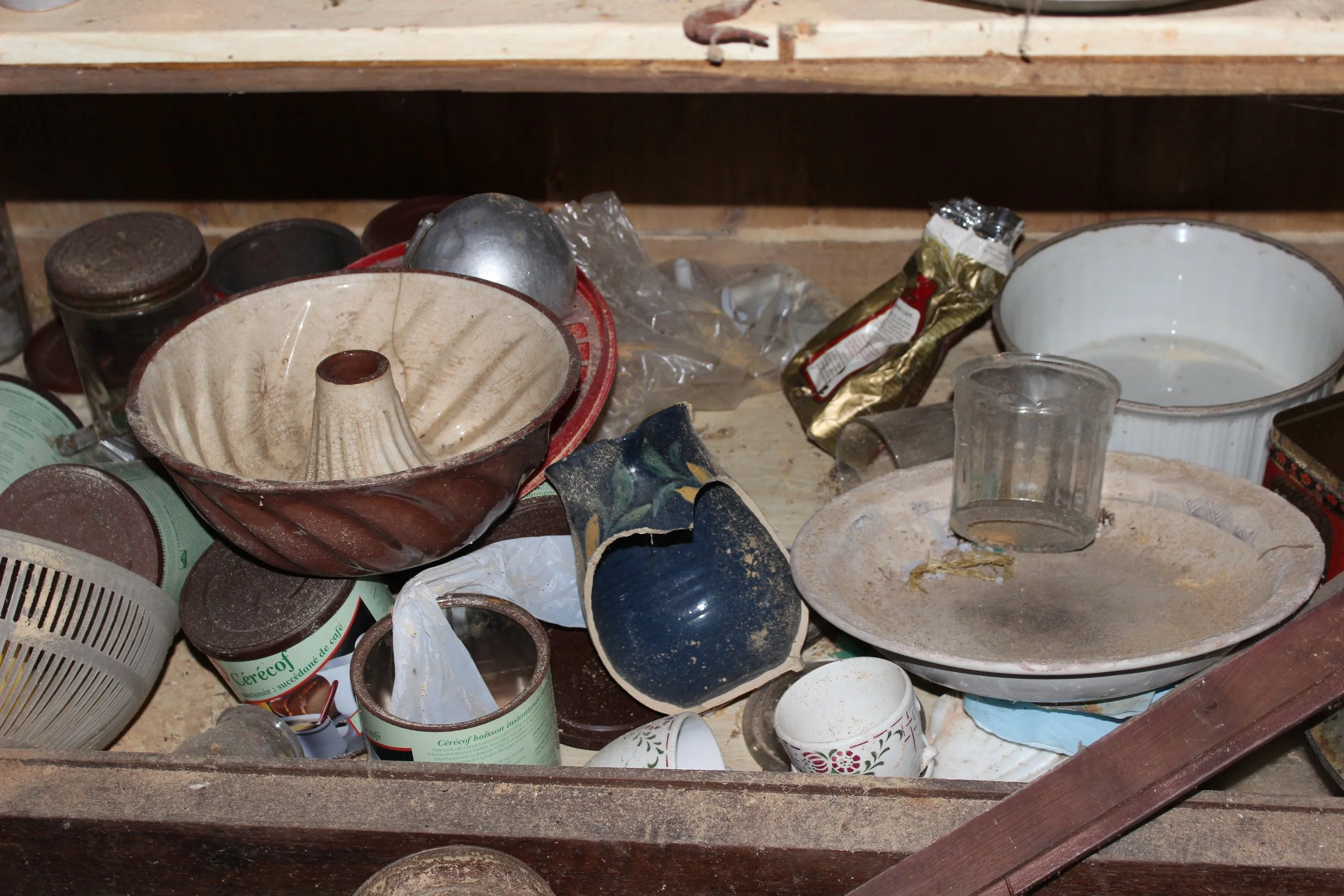 Haufen schmutziger Geschirrteile, inklusive Schüsseln, Tassen, Dosen und Besteck, auf einem Holzregal.