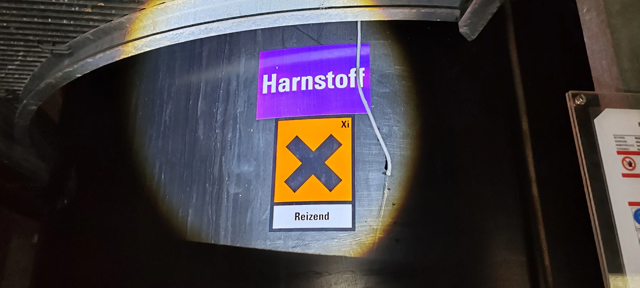 Ein Schild mit dem Namen 'Harnstoff' in lila und ein Warnschild mit einem schwarzen Kreuz auf orangeem Hintergrund, das die Gefahr durch reizende Substanzen kennzeichnet.