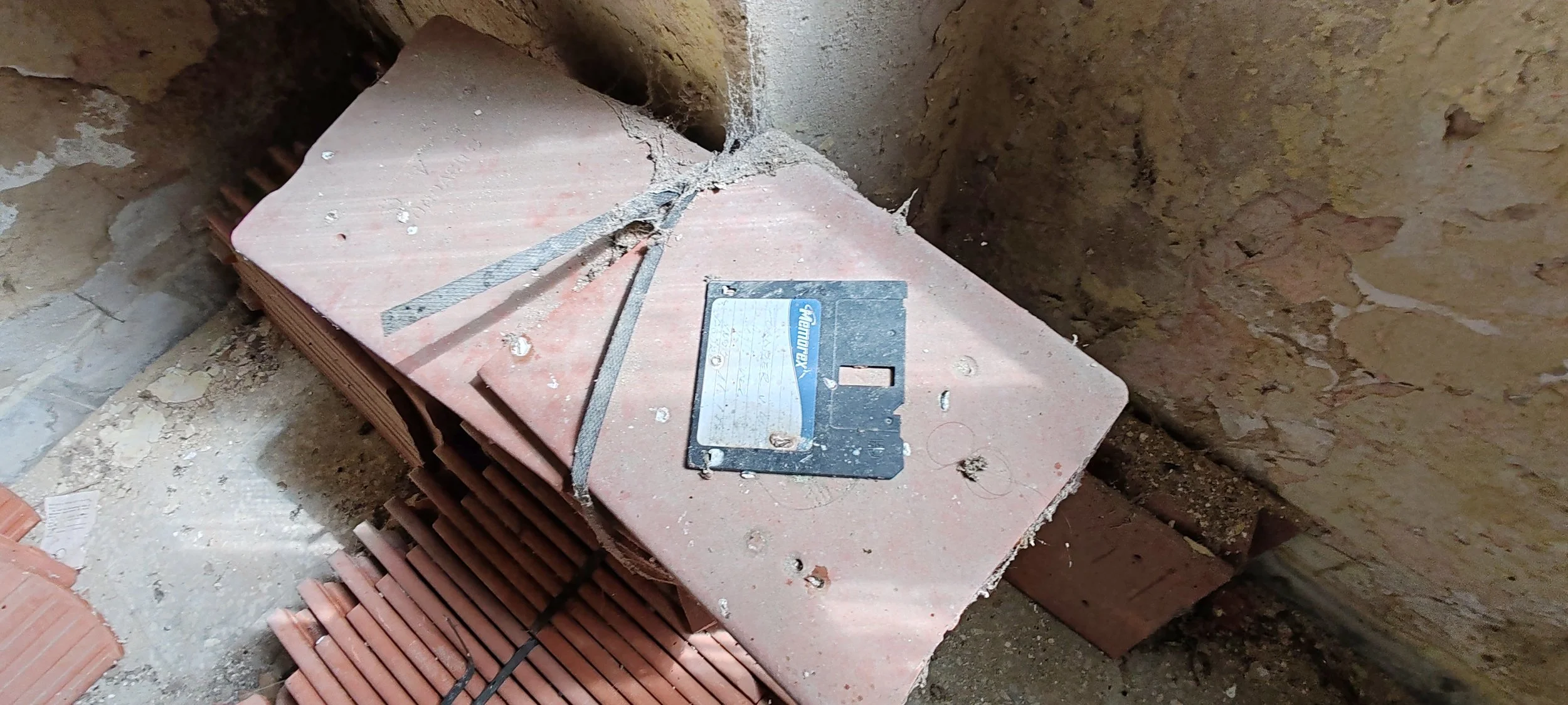 Baustelle mit roten Ziegelsteinen, ein Steinmesser, und eine Steinplatte mit Metallmarkierung, umgeben von Mauerwerkswänden und Bauschutt.