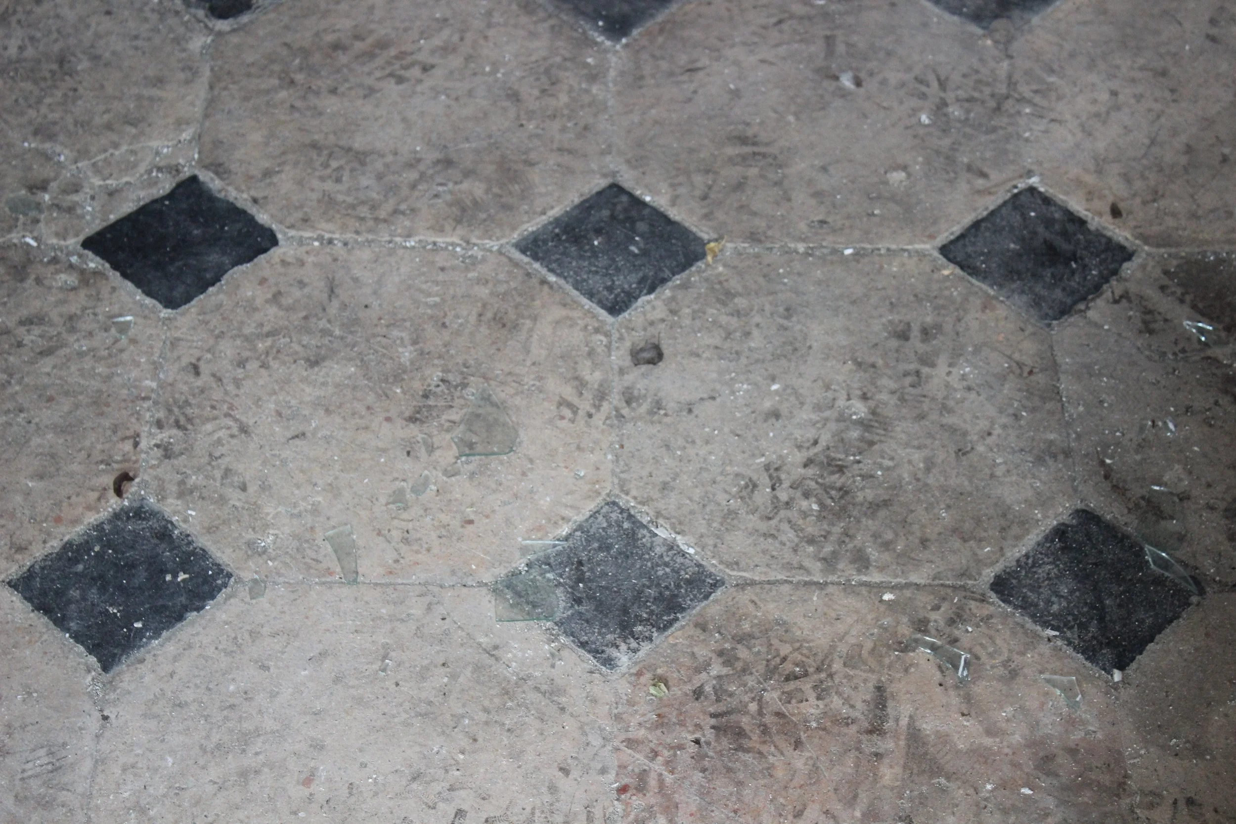 Bodenbelag mit beige und schwarze Fliesen, einige Fliesen sind zersplittert.