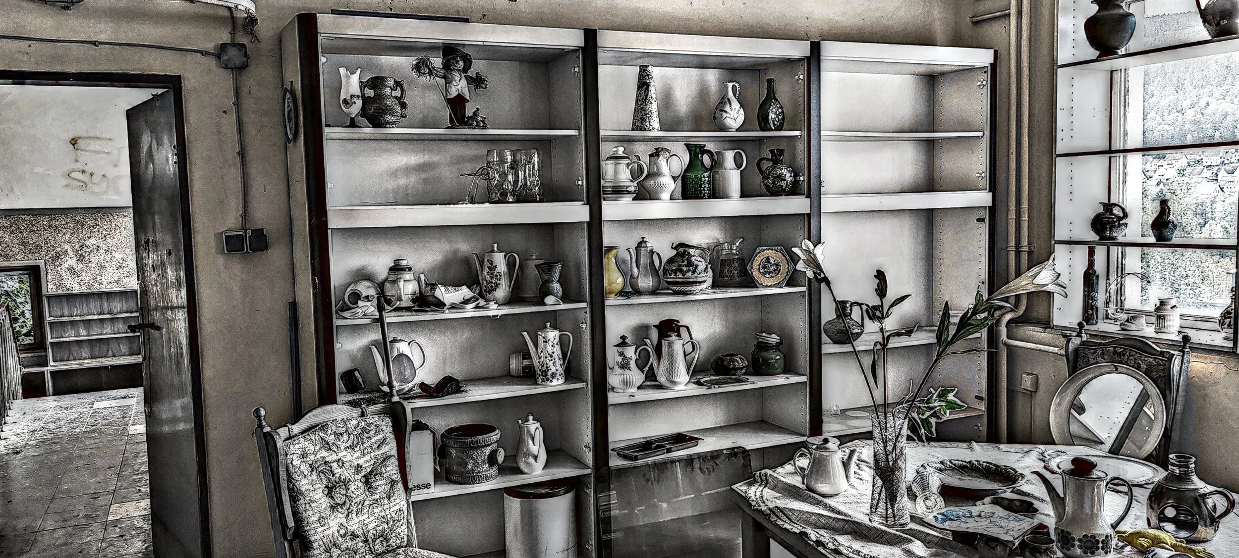 Ein Raum mit leeren Bücherregalen, einem Tisch mit Vase und Geschirr, einem Fenster mit Schneefall im Hintergrund, und einem Stuhl, alles in einem alten, etwas verfallenen Haus.