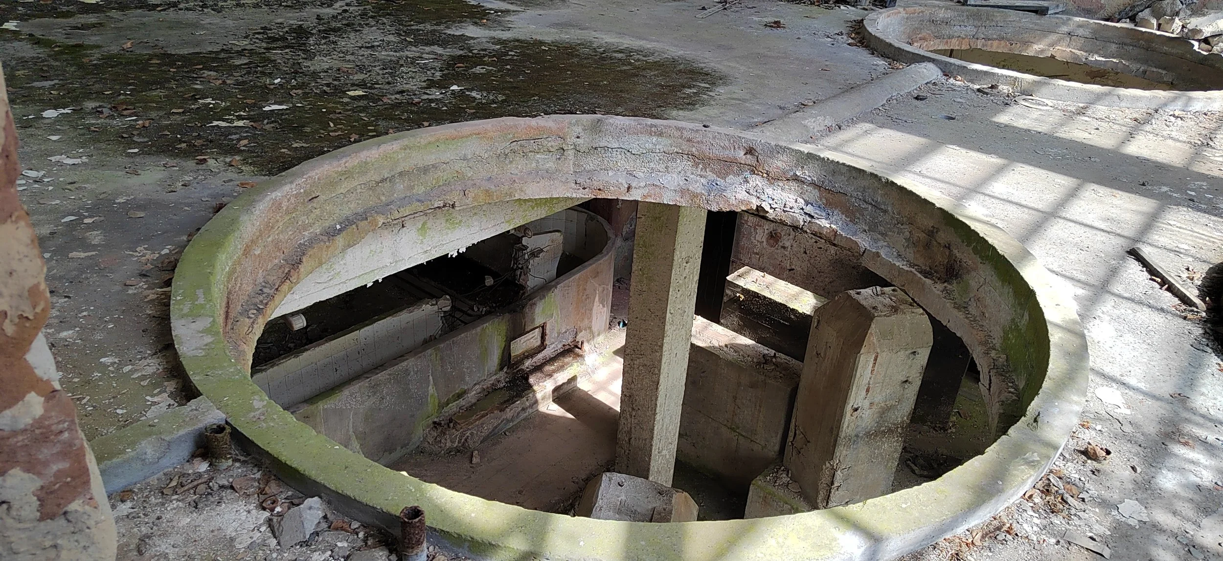 Rundes, altes Brunnengesicht mit grüner Moosbedeckung, im Inneren sichtbare Stein- und Ziegelstrukturen, im Sonnenlicht geflimmert.