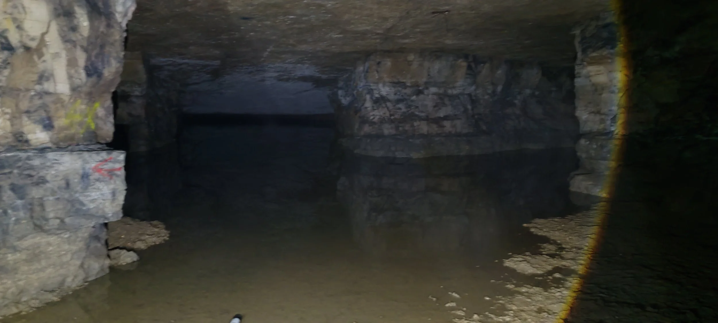 Ein dunkler Höhleneingang mit Wasser im Vordergrund, umgeben von steinernen Wänden.