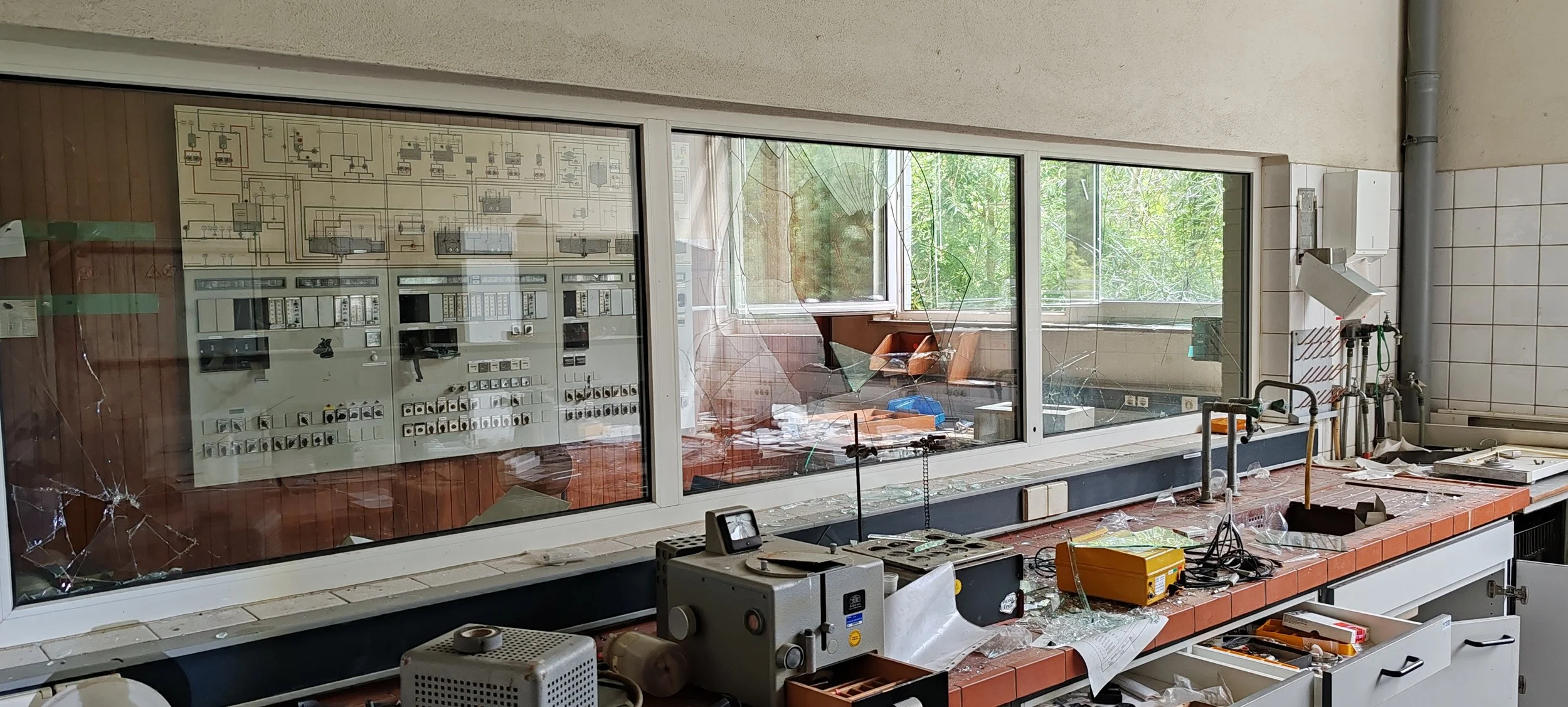 Zerstörtes Labor mit zersplitertem Fenster, zerbrochenen Gläsern und beschädigten Geräten.