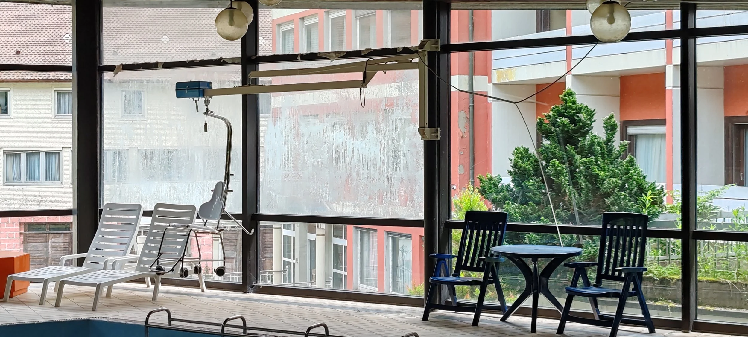 Blick auf eine verglaste Ostsee mit Liegestühlen, einem Tisch und Stühlen, sowie einem Rollstuhl und einer Sonnenbank