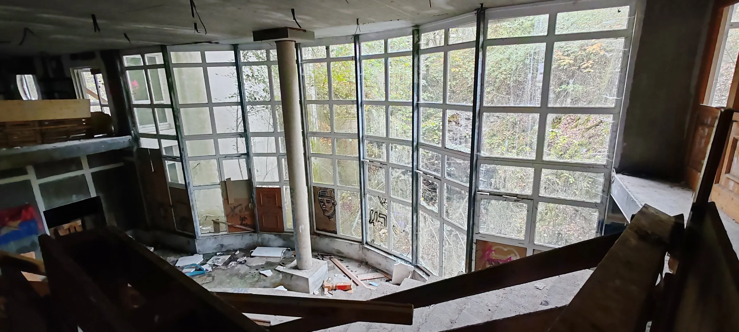 Ein verlassener, unvollendeter Innenraum eines Gebäudes mit großen Glasfenstern, Baugerüsten und Graffiti an den Wänden.