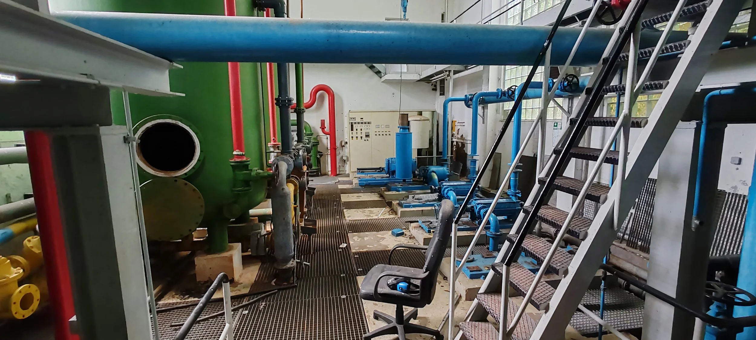 Anlagenteile und Rohrleitungen in einer technischen Einrichtung, vermutlich in einem Kraftwerk oder einer industriellen Anlage, mit Metalltreppe und Arbeitsplatz.