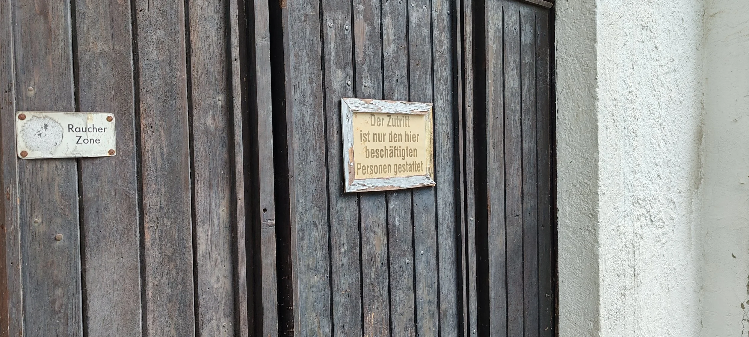 Holztür mit zwei Schildern, eines liest 'Raucher Zone' und das andere bedeutet, dass nur dort die Zutrittsberechtigung für Beschäftigte gilt.