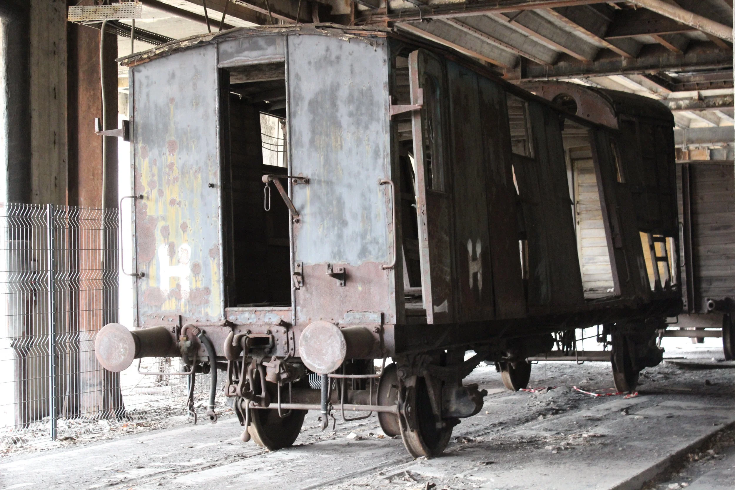 Ein verrosteter, alter Eisenbahnwagen steht in einer Bahnstation oder Lagerhalle, umgeben von Staub und Schmutz.