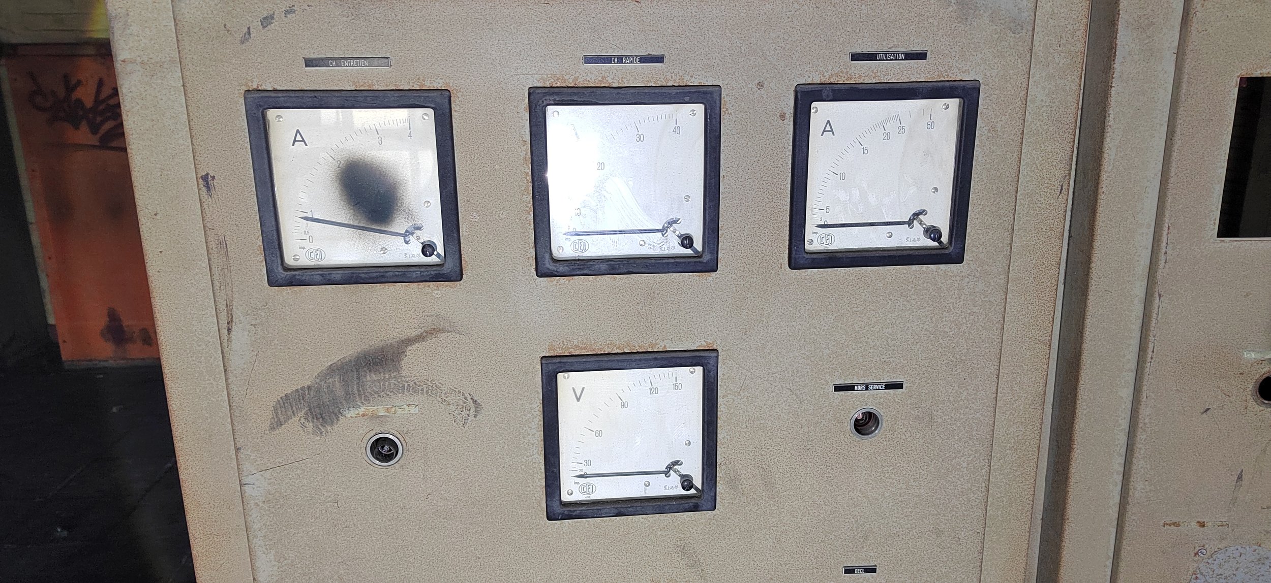 Alte, verrostete Steuerungseinheit mit drei analogen Messinstrumenten für Strom und Spannung, die in einem industriellen Umfeld angebracht ist.