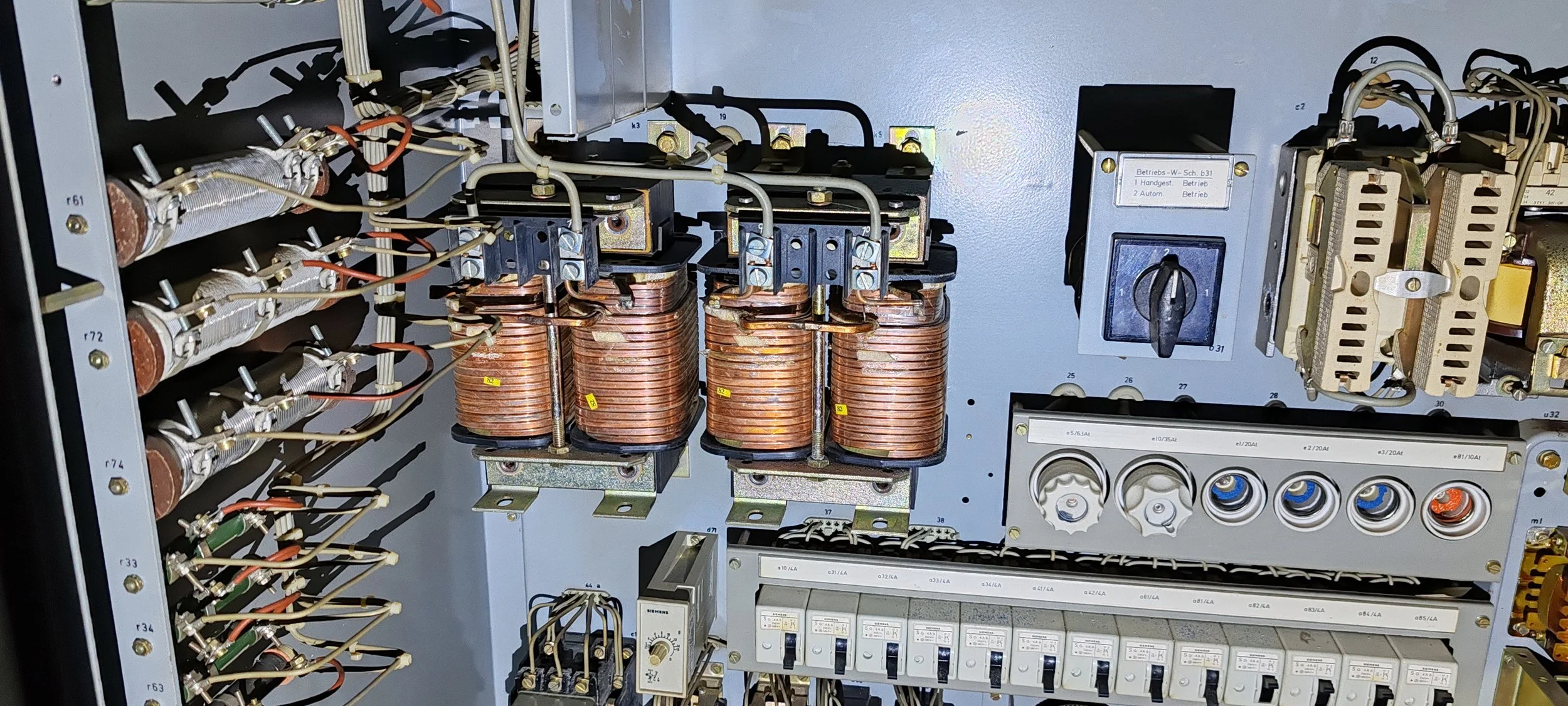 Innere Komponenten eines elektrischen Schaltschrankes, inklusive Spulen, Widerständen, Schaltern und Sicherungen, angeordnet auf einer Metallplatte.