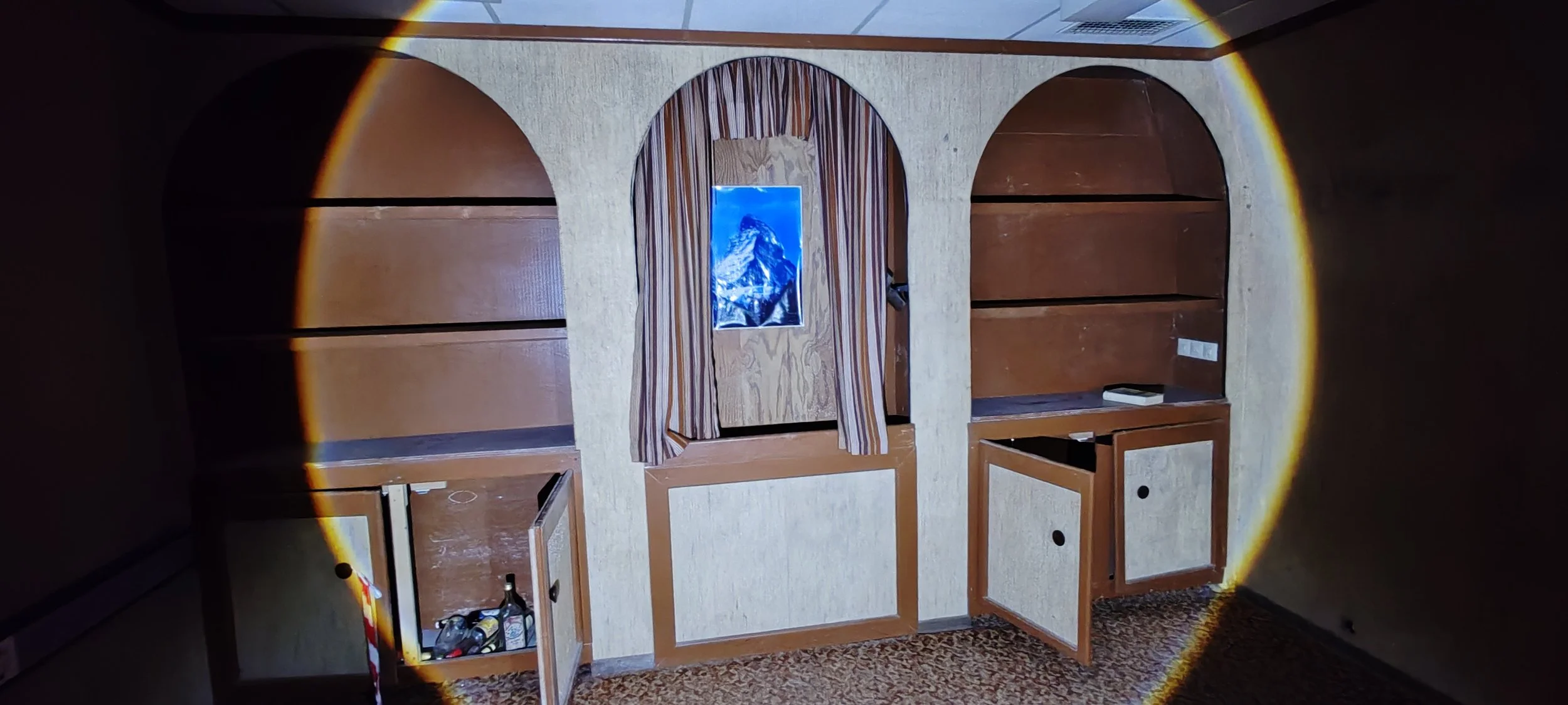 Leeres Holzregal in einem dunklen Raum, projiziert haben, ein Sonnenuntergang, eine kleine Tür mit Vorhang und eine kleine Tafel mit einem Bergbild davor.