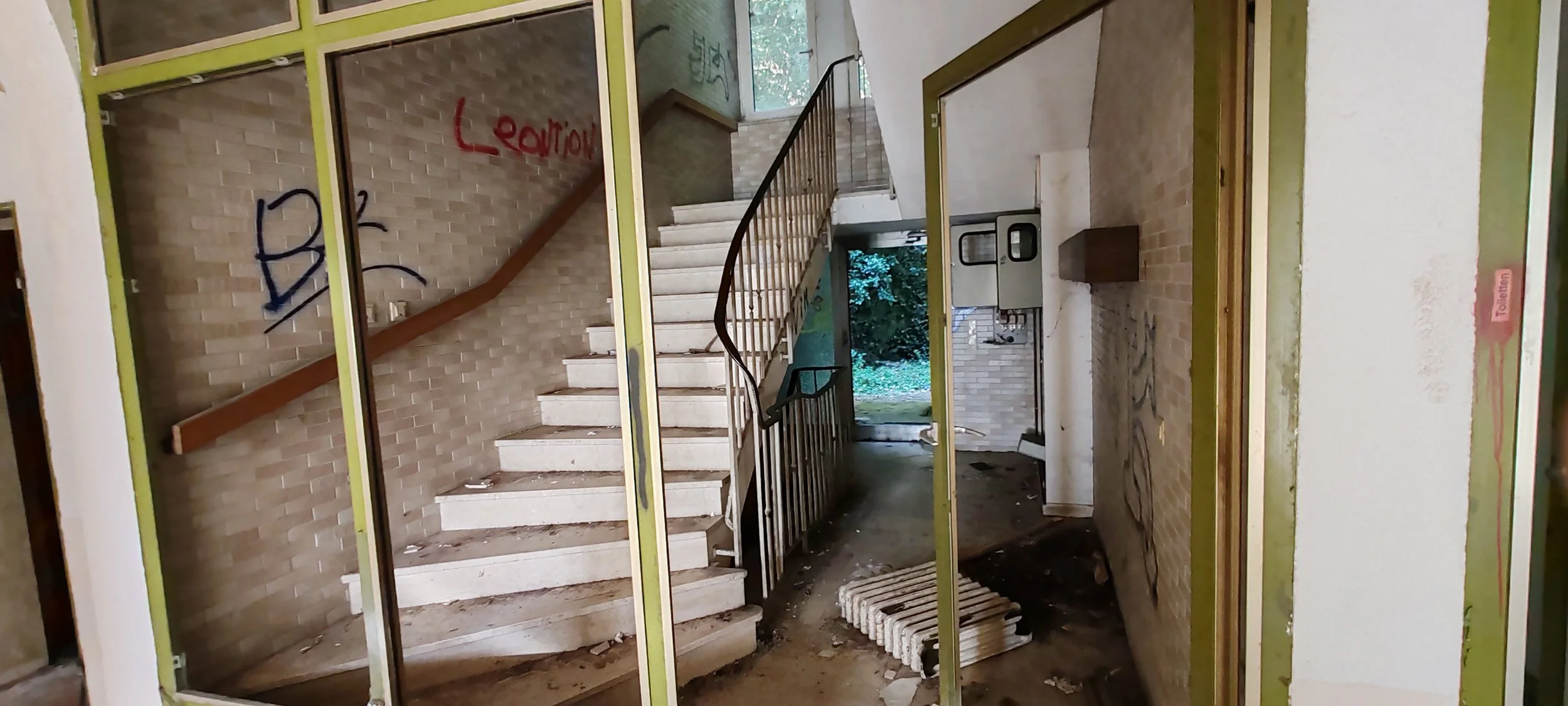 Der Eingang eines verlassenen Gebäudes mit einer Treppe und unordentlichem Innenraum, Graffiti an den Wänden und Bauarbeiten an der Wand.