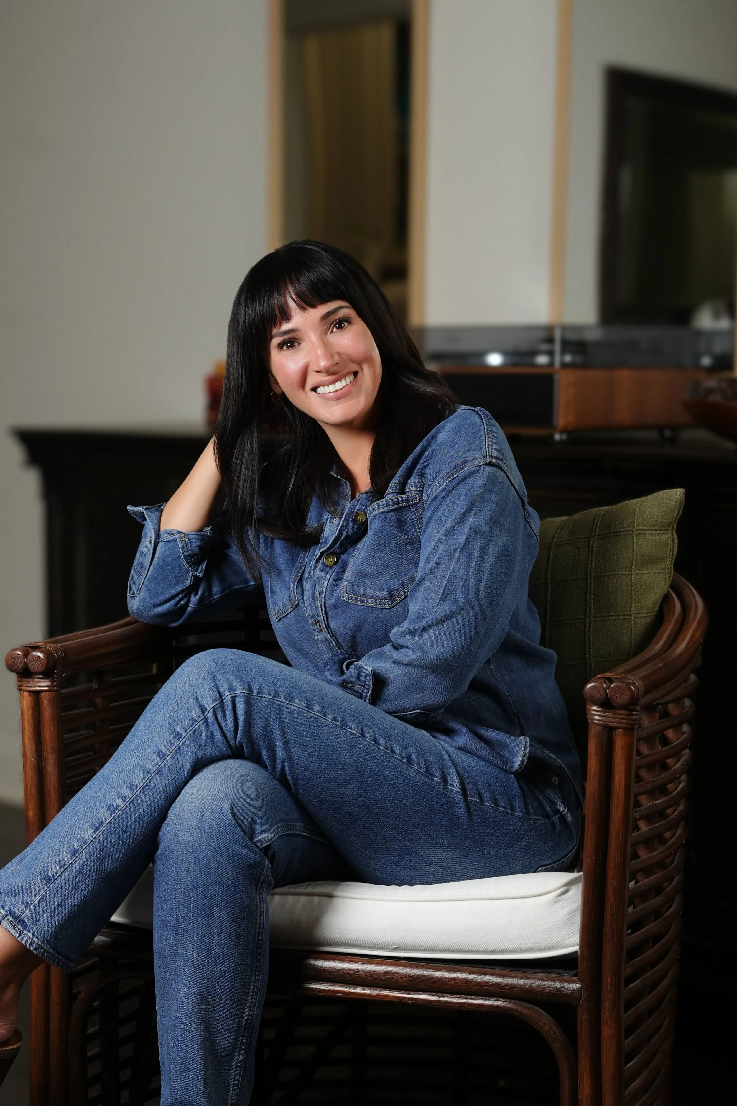 Maegan Jones, LCSW, smiling in a denim shirt with her hand in her hair, seated in a chair in a warmly lit room