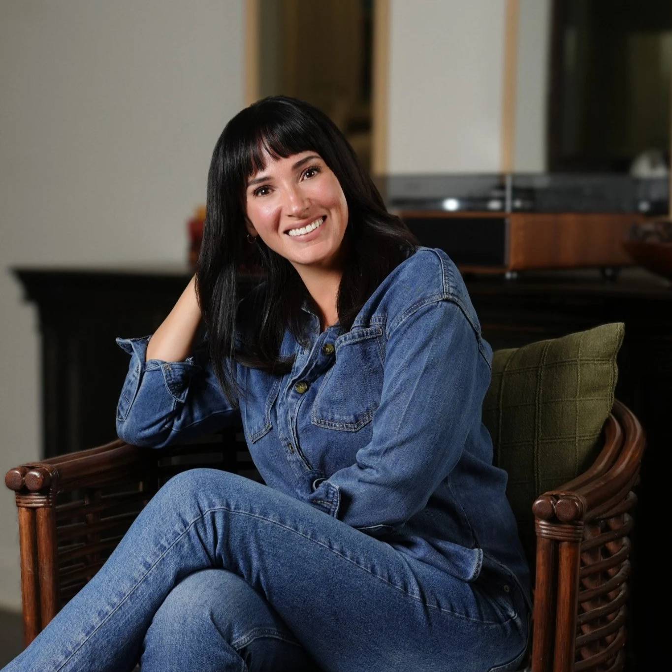 Maegan Jones, LCSW, smiling in a denim shirt with her hand in her hair, seated in a chair in a warmly lit room