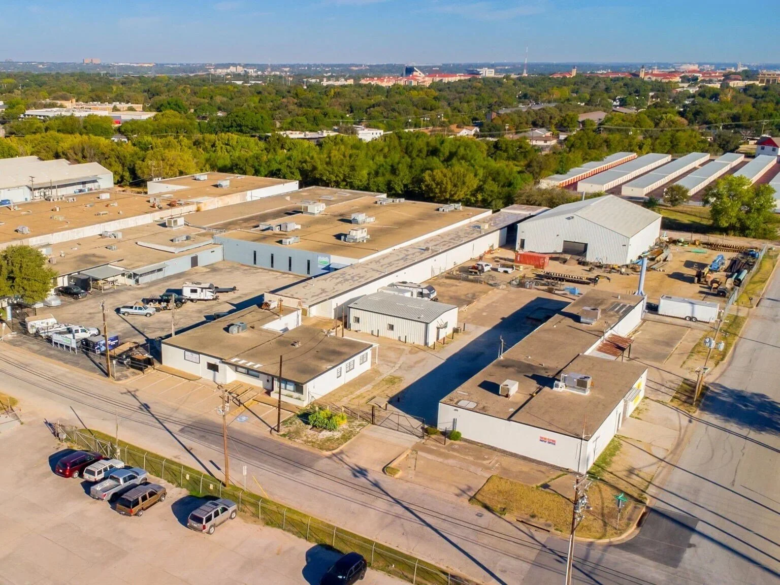 Aerial view of an industrial area in North Texas with multiple warehouses, storage units, and parking lots, surrounded by trees and a residential neighborhood in the background.