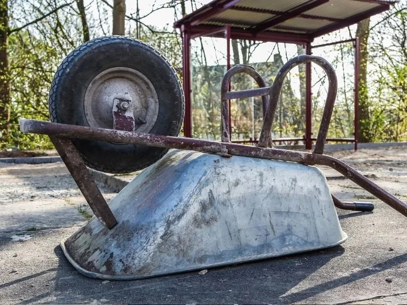 An old, rusty wheelbarrow lying on its side on the ground, an example of a small sandblasting project that could be done better and more eco-friendly with dustless blasting.
