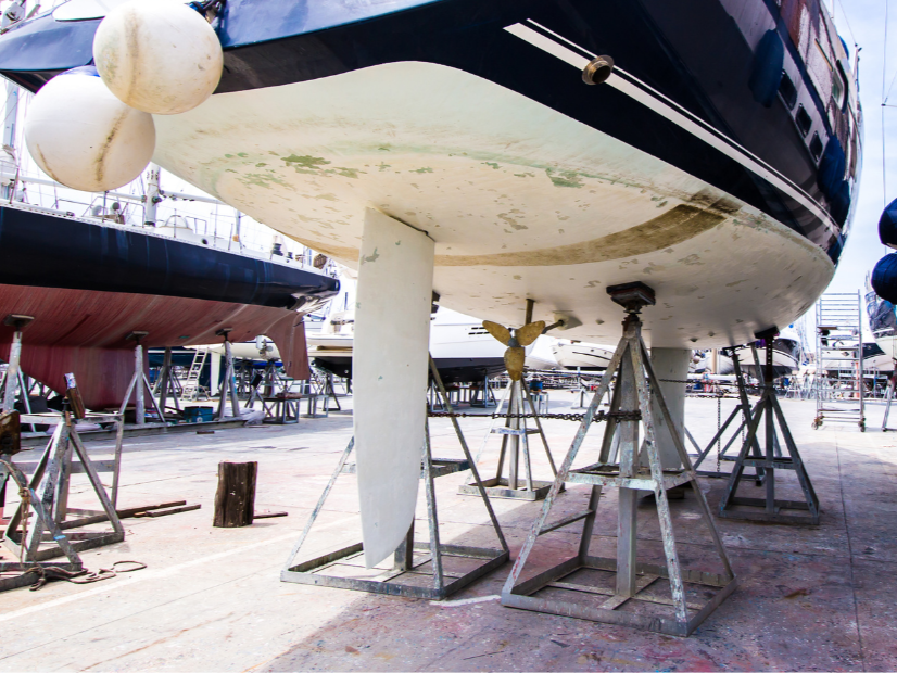 View of a boat in a boatyard on stands for maintenance or repairs, with other boats and equipment in the background as it is prepared to be cleaned by Ready Surface.