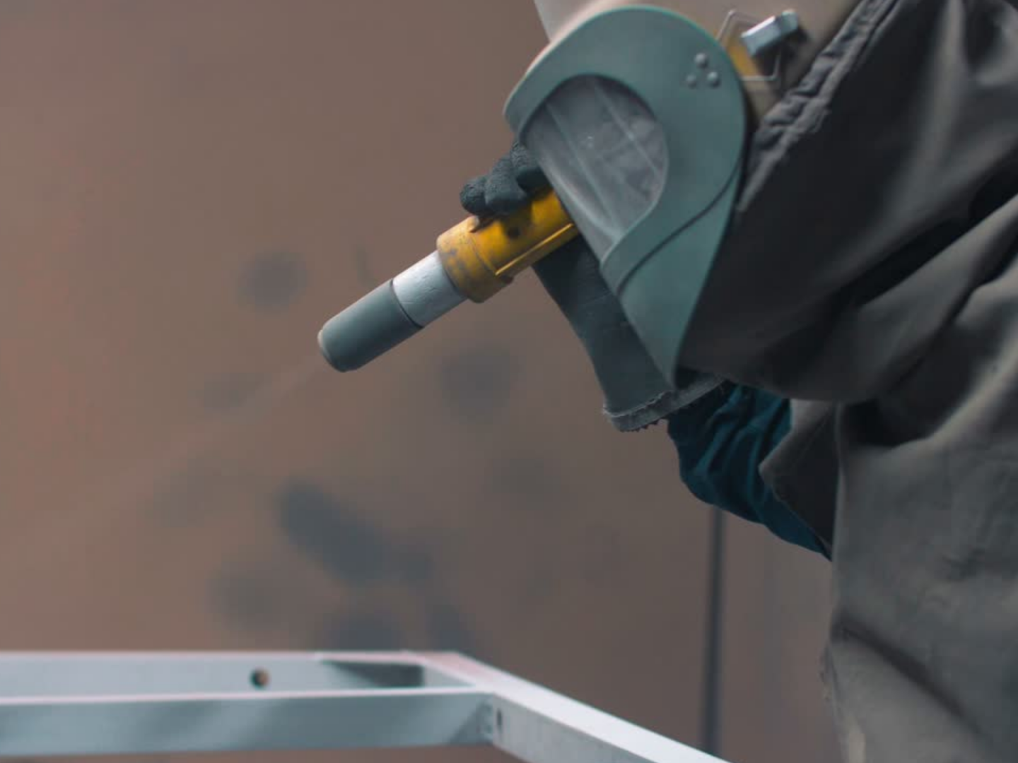 Person wearing protective gear using a sandblasting or dustless blasting nozzle to clean paint off metal surface in North Texas