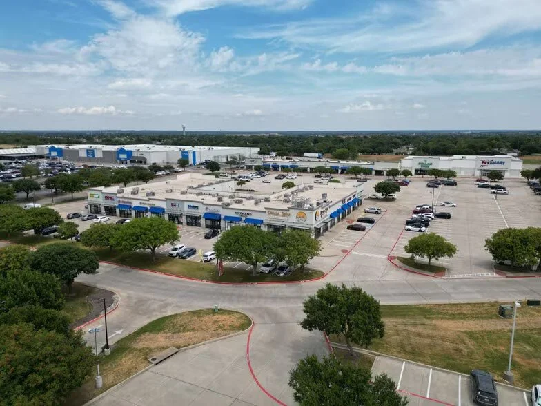 A large shopping plaza with multiple retail stores, parking lot with cars, surrounded by trees, under a partly cloudy sky that is well kept preserving the value of the property using clean up by Ready Surface and dustless blasting.