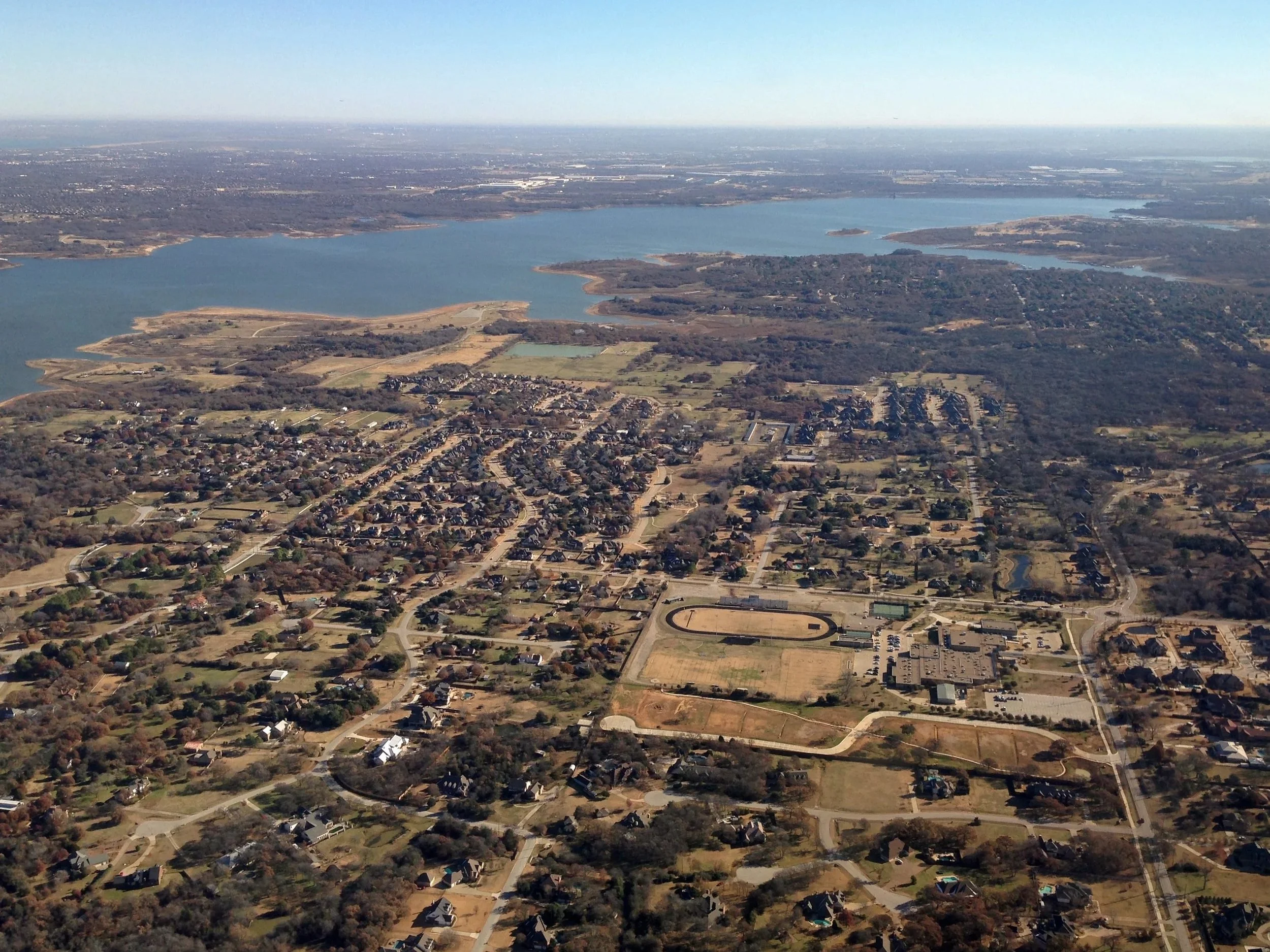 Aerial view of a suburban area near a large lake with greenery and residential neighborhoods.